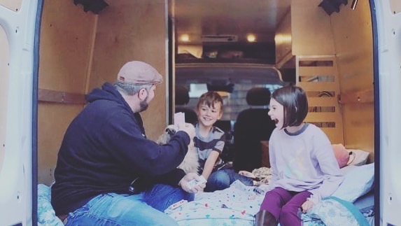 Family enjoying time in their RV rental! A dad, two kids, and dog laugh and play inside their camper van.. RAM ProMaster 2022