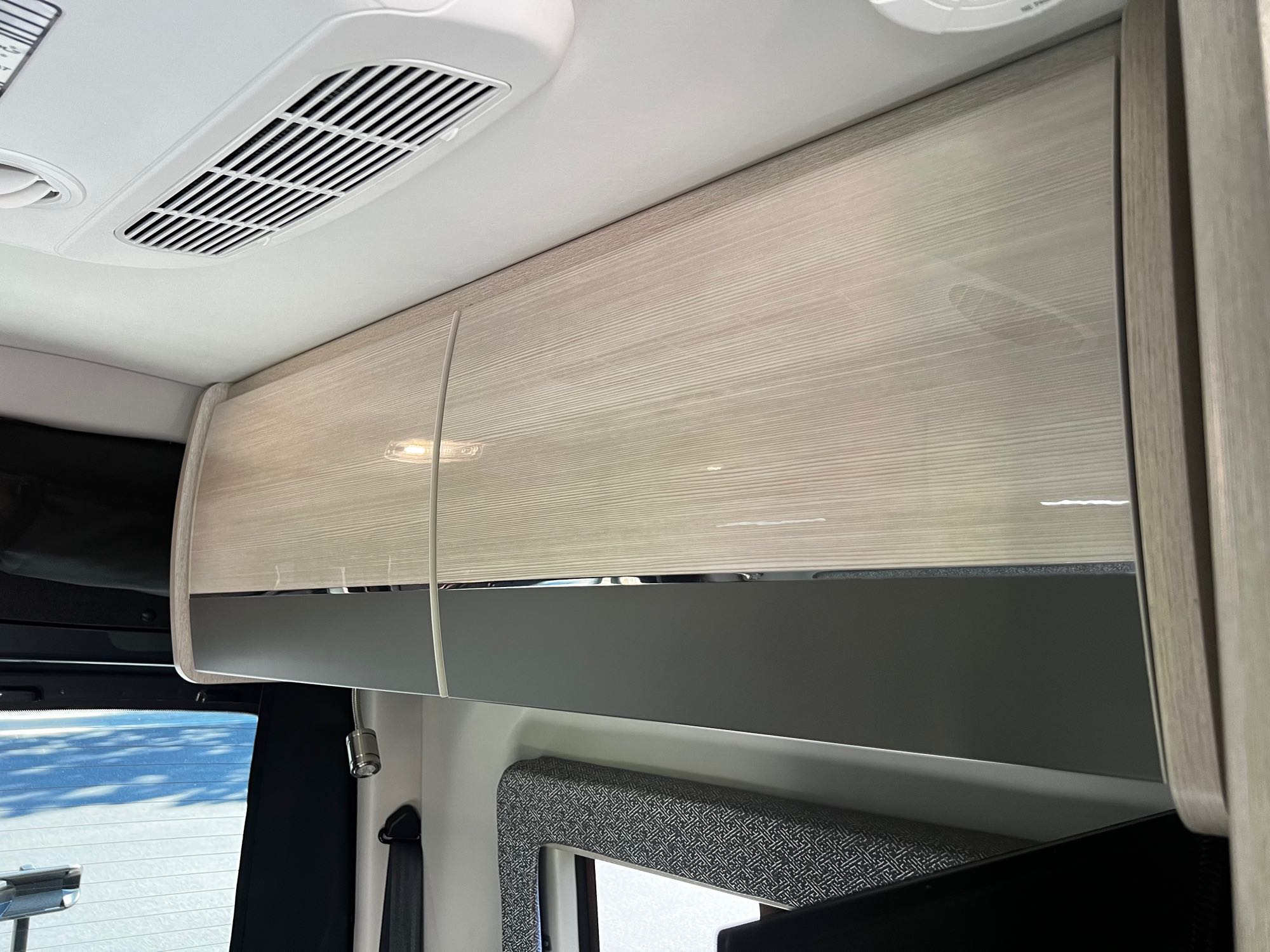 Modern RV rental interior with light wood overhead cabinets, ceiling air vent, and reading light for comfort.. Thor Motor Coach Tranquility 19P 2023