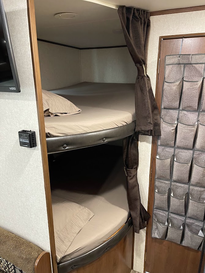 View of cozy RV rental bunk beds, neatly made with light sheets. Dark privacy curtains and a hanging organizer offer compact comfort.. Jayco Jay Flight SLX 2017