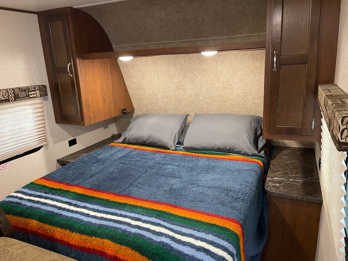 Cozy RV rental bedroom with a colorful blanket, gray pillows, and overhead storage for comfortable travel.. Jayco Jay Flight SLX 2017