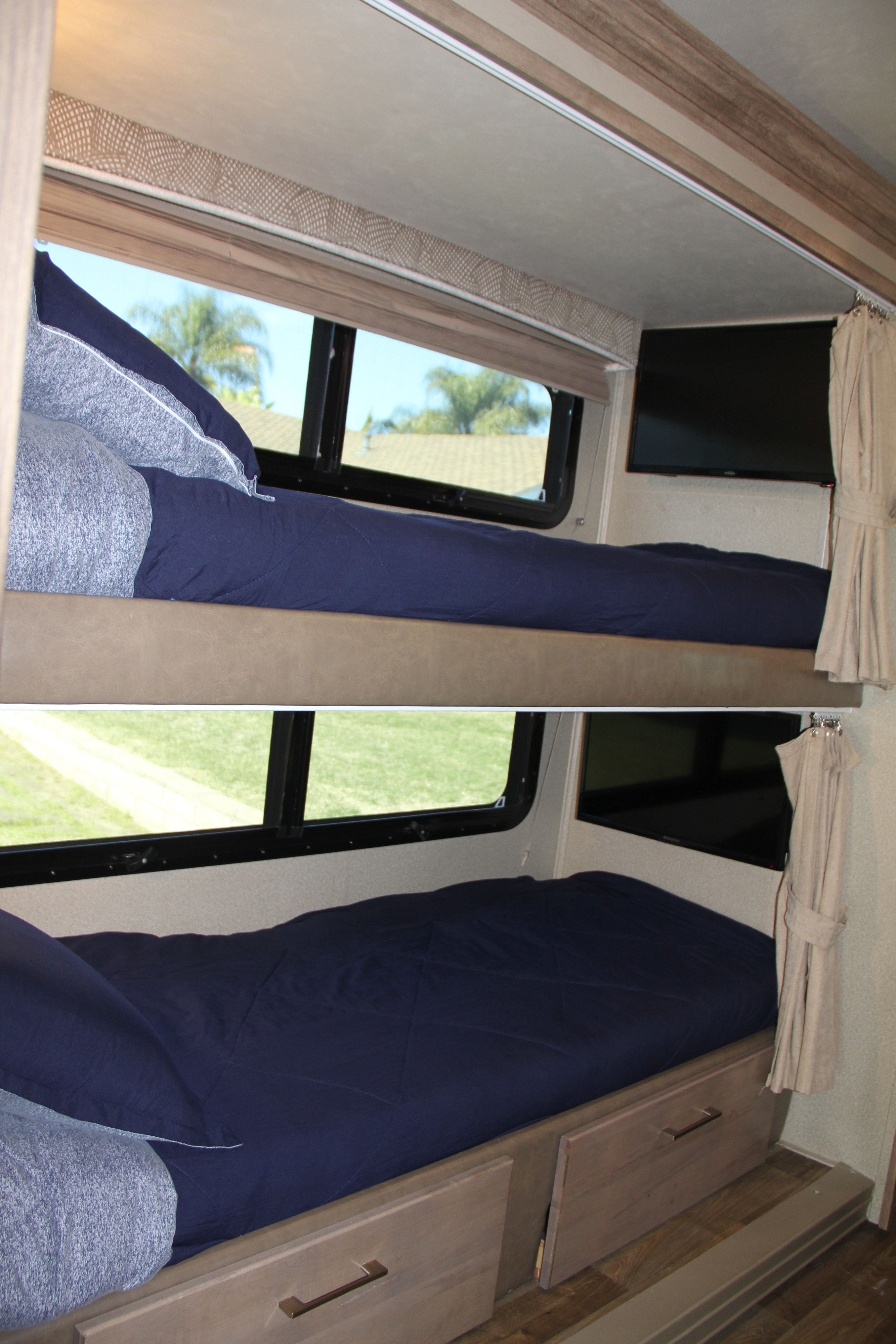 RV rental bunk beds with navy blue bedding, windows, TV, and under-bed storage drawers in a motorhome.. Entegra Coach Odyssey 2019