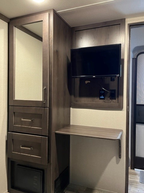 RV rental's functional interior: mirrored wardrobe, storage drawers, mounted TV, and a convenient desk.. Grand Design Reflection 2020