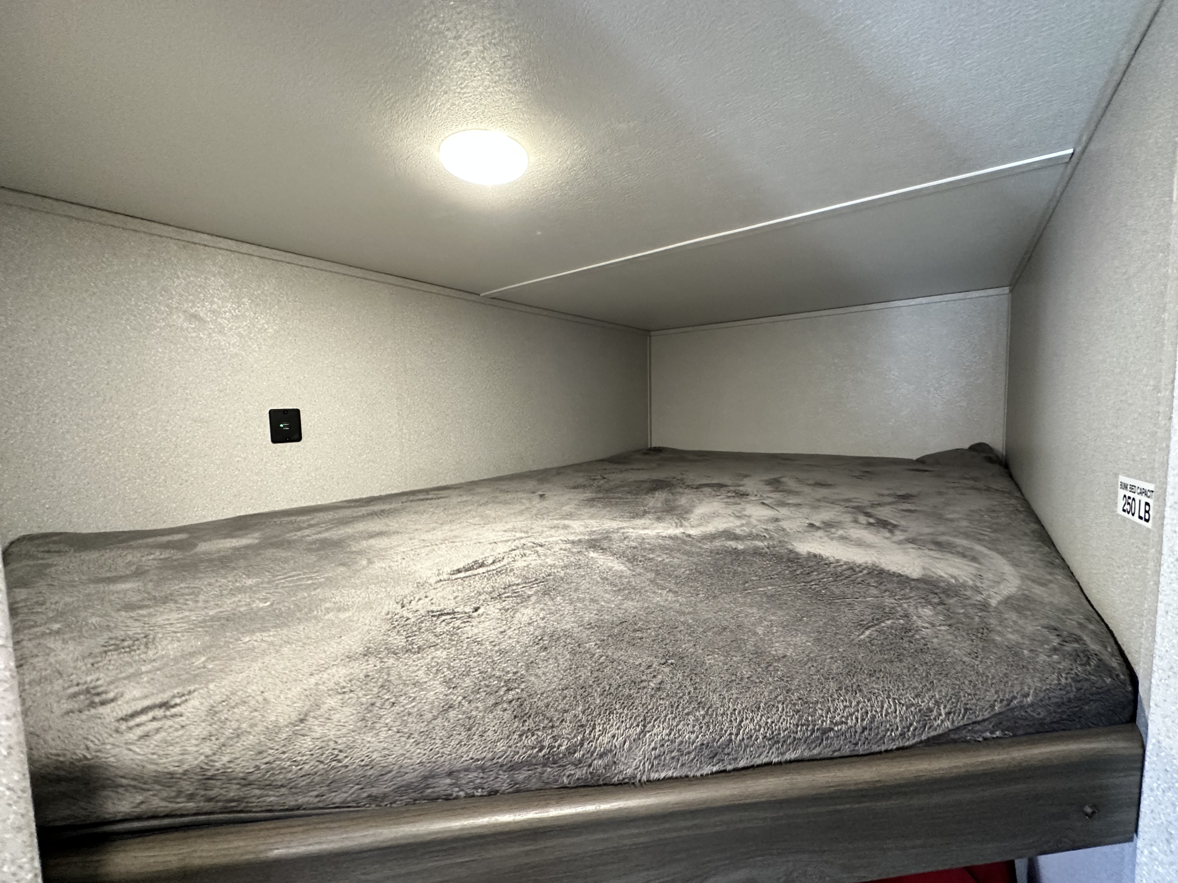 Cozy RV rental bunk bed, ready for a restful night. Features include a ceiling light, USB port, and 250 LB capacity.. Shasta 26BH 2021