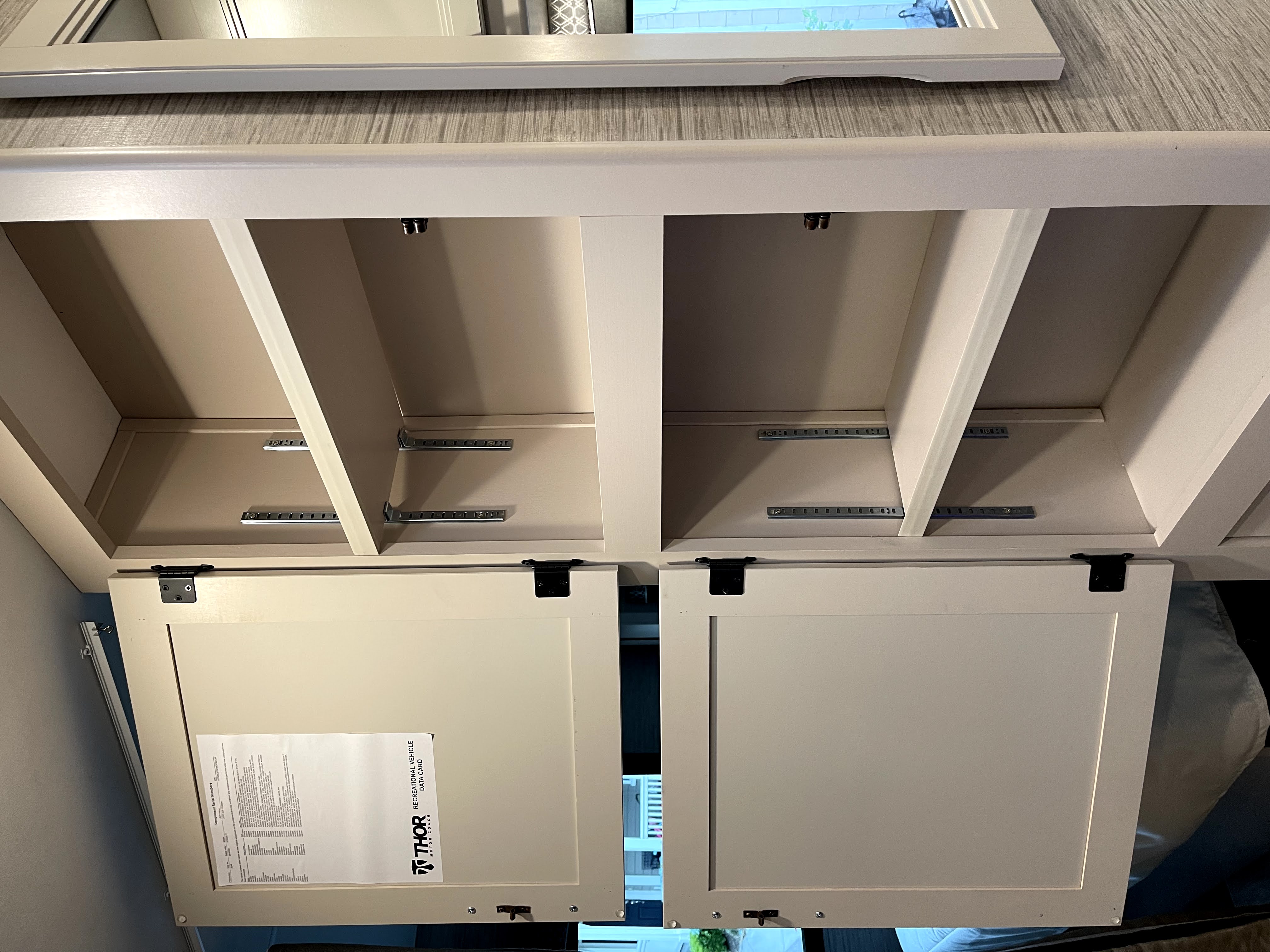 Inside an RV rental: open overhead cabinets reveal adjustable shelves for storage. A Thor Motor Coach data card is visible.. Thor Chateau 2022