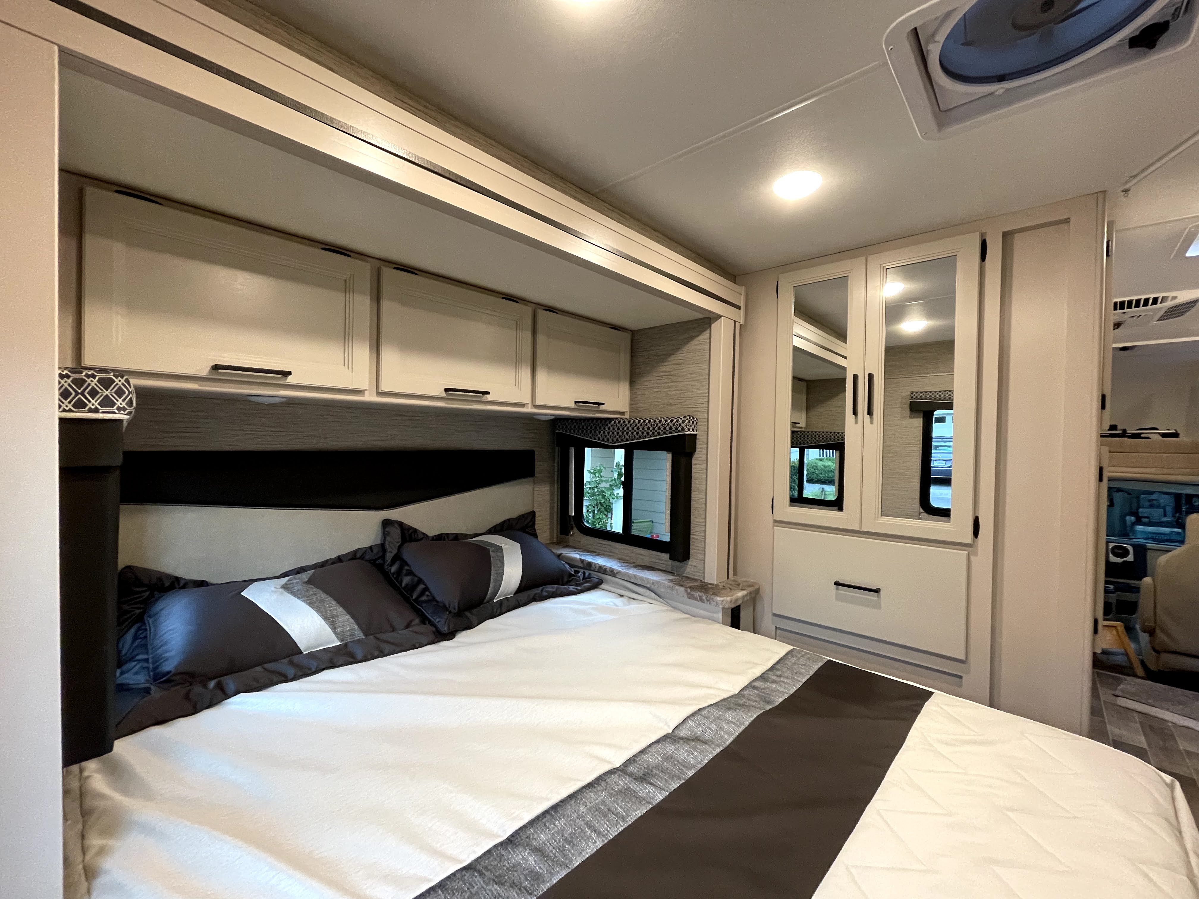 Modern RV rental bedroom: a bed with patterned bedding, overhead cabinets, and mirrored closet. Cozy travel.. Thor Chateau 2022