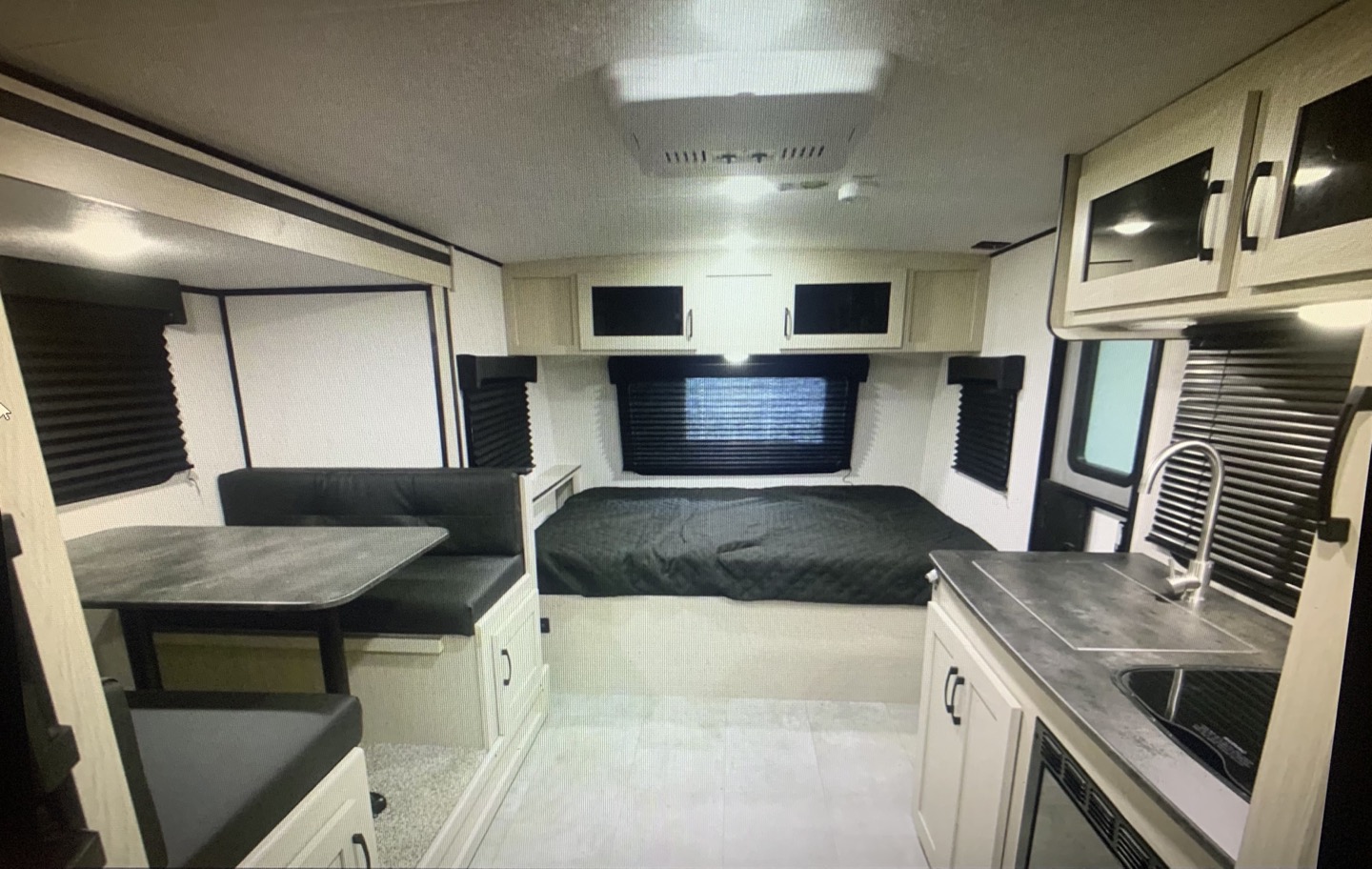 Spacious RV rental interior featuring a cozy bed, a dinette to the left, and a compact kitchen on the right.. Coachmen Apex Nano 2021