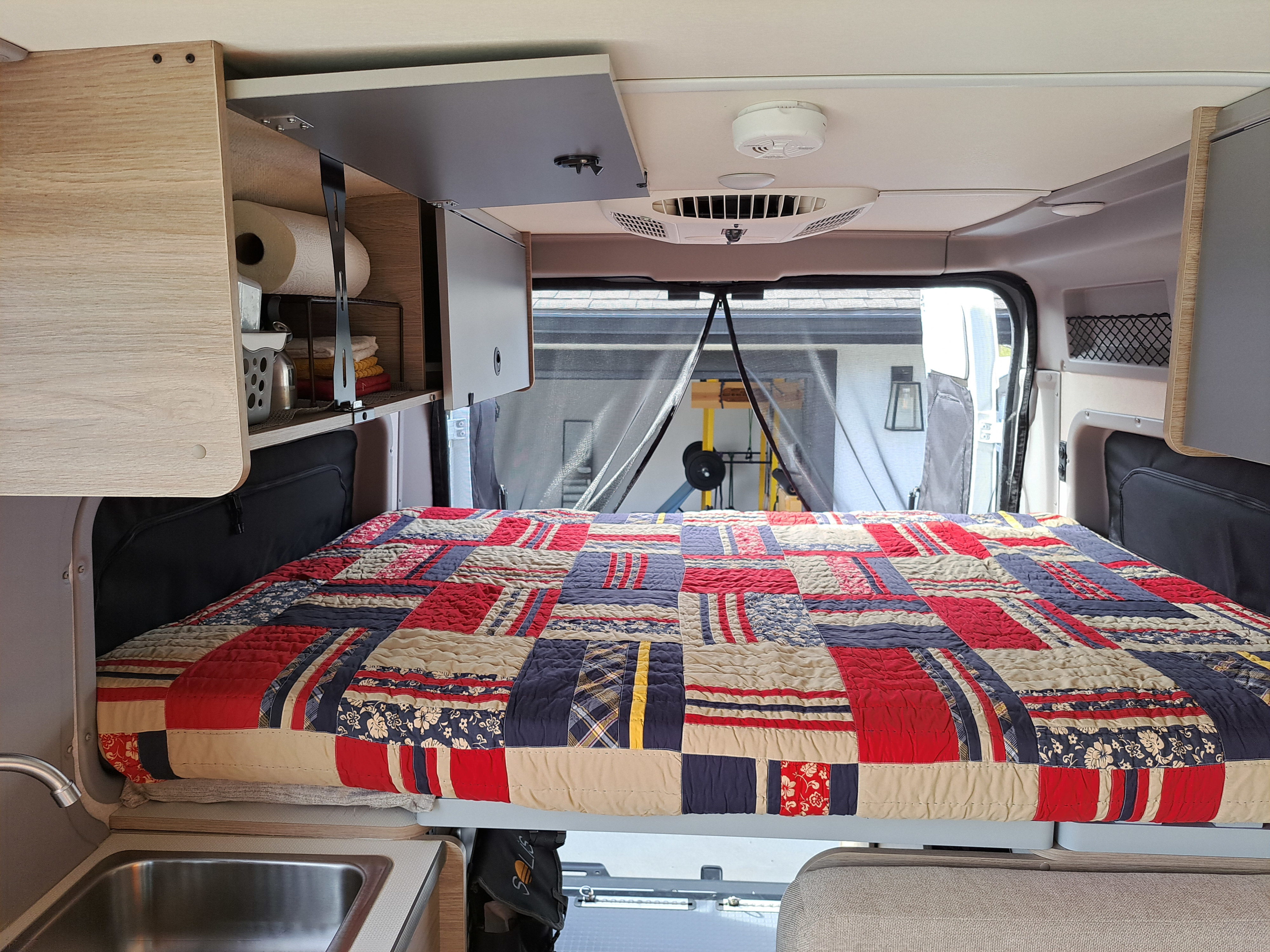 RV rental interior featuring a cozy bed with a colorful quilt, kitchenette, and overhead storage, perfect for travel.. Winnebago Winnebago 2023