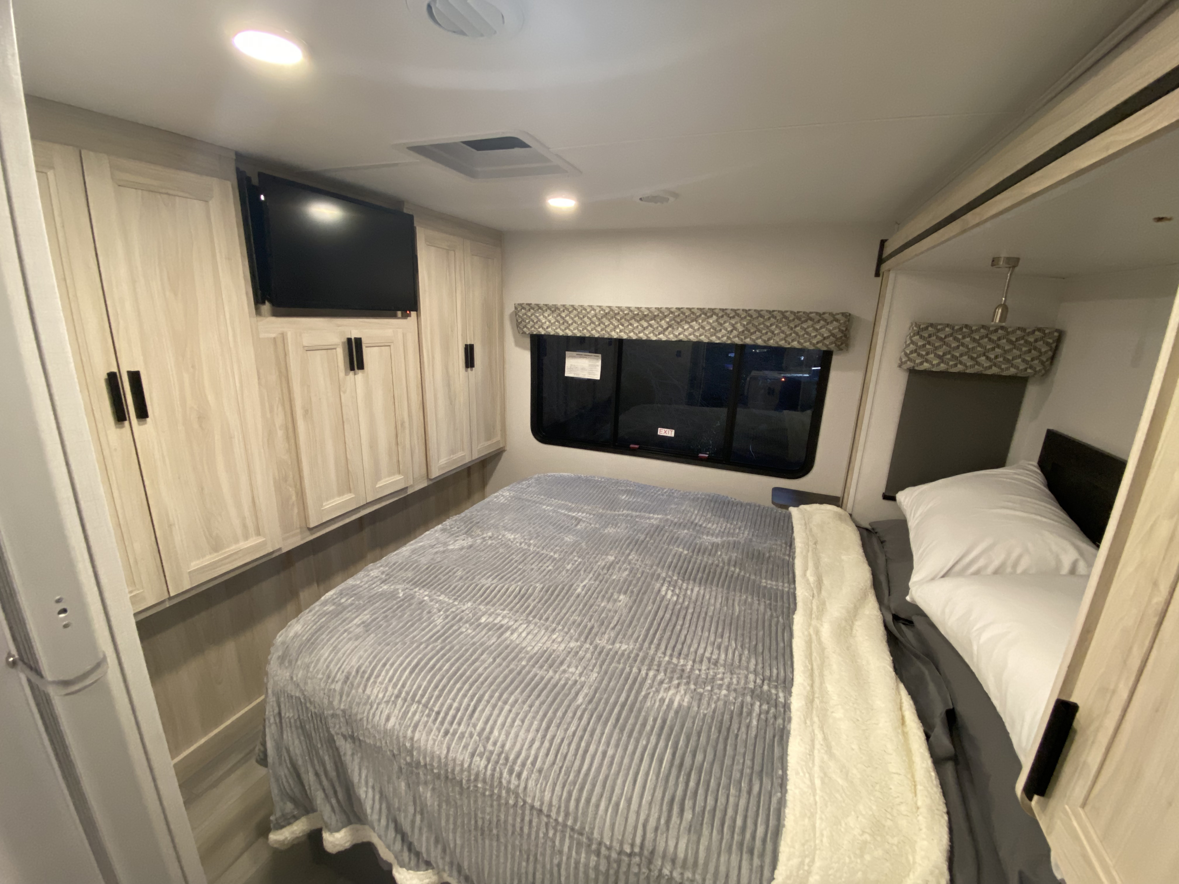 Step into comfort! This RV rental bedroom features a cozy bed, TV, and stylish light wood cabinetry, perfect for your journey.. Forest River Forester 2023
