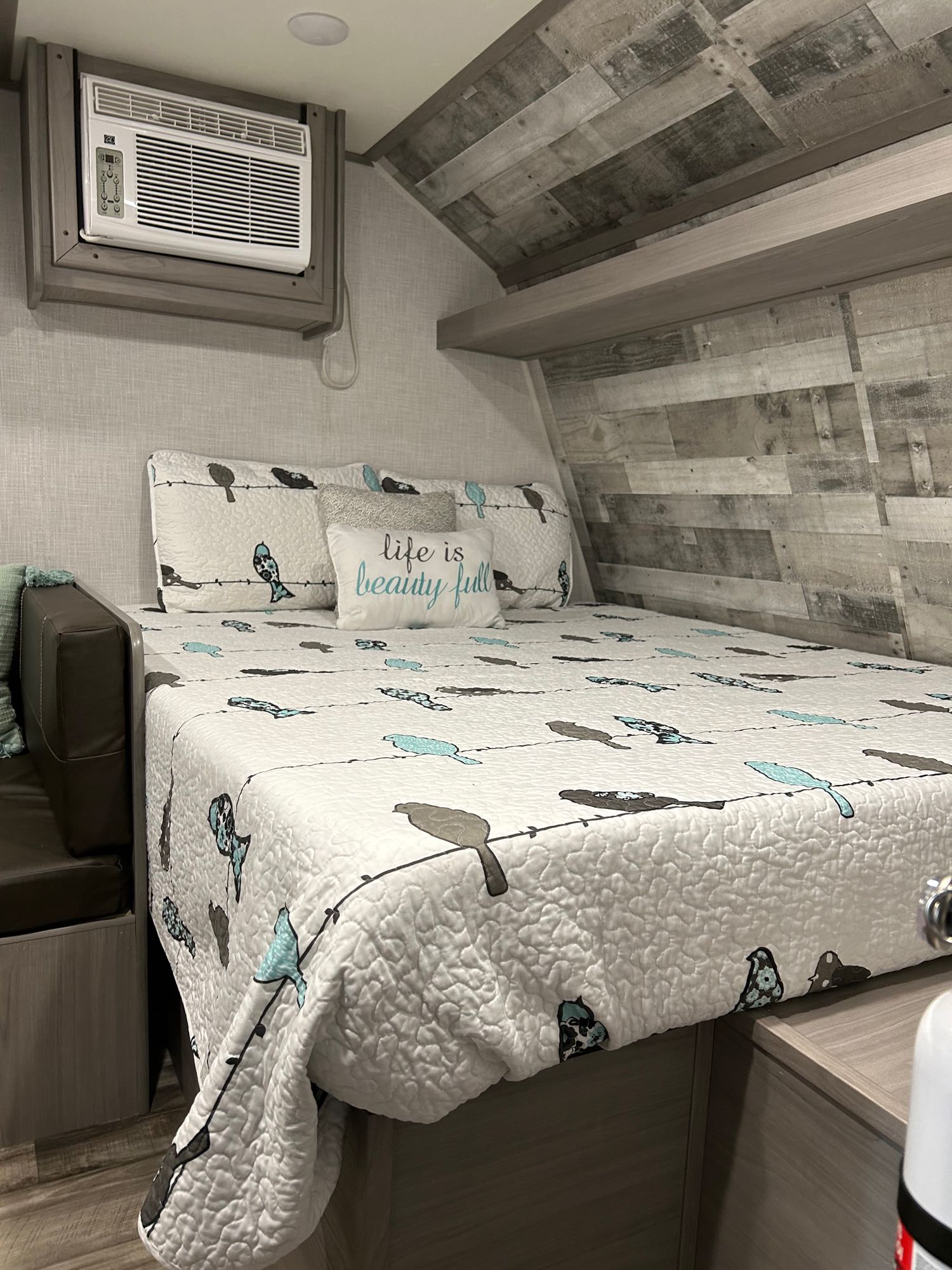 Cozy RV rental bedroom with bird-themed bedding, an AC unit, and distressed wood decor. Ideal for comfortable travel.. Dutchman Coleman 17 B 2023