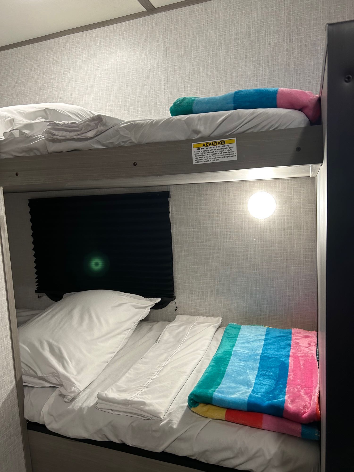 Inside an RV rental, comfortable bunk beds feature white linens and vibrant blankets.. Dutchman Coleman 17 B 2023