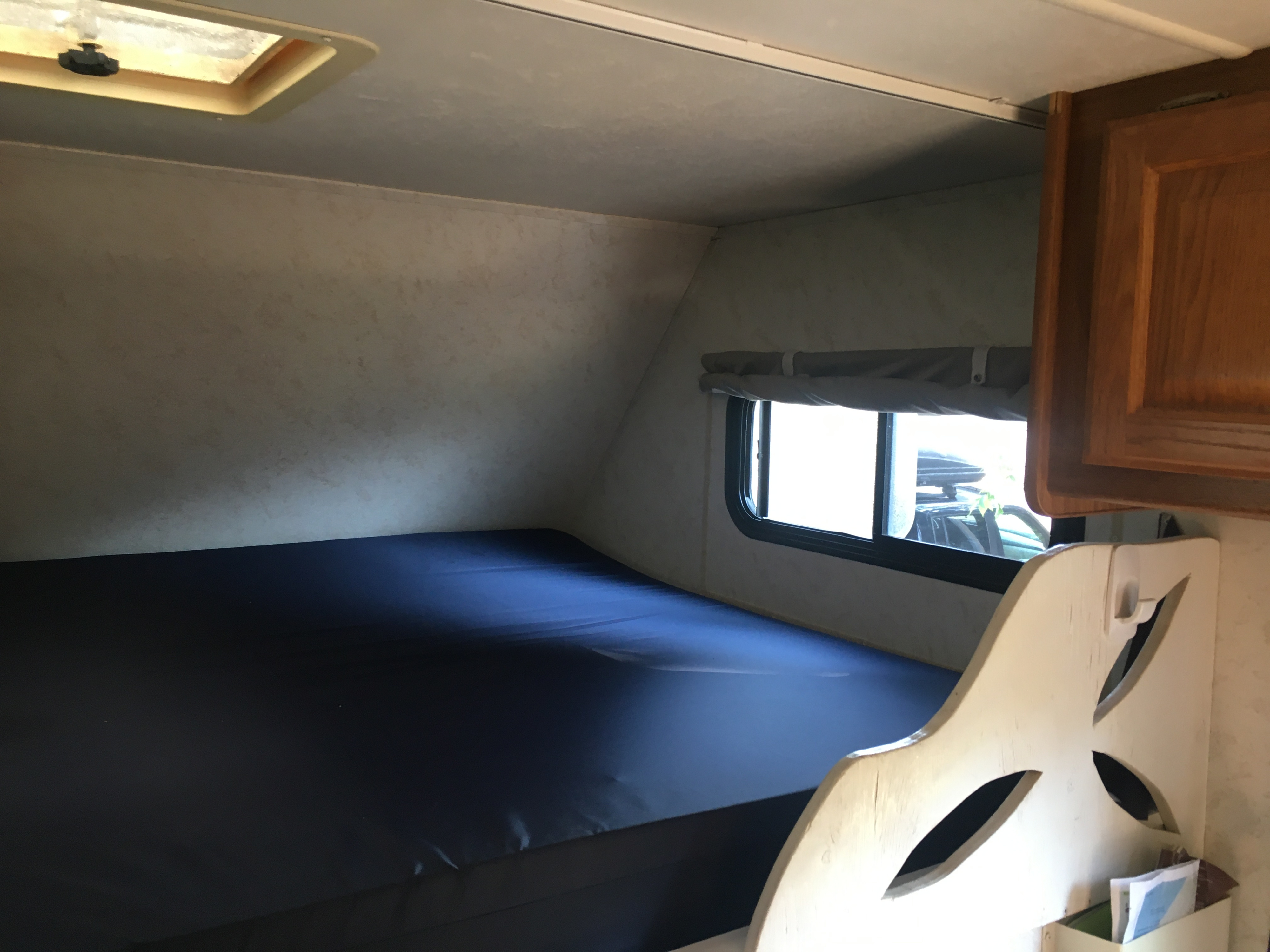 An RV rental interior showing a bed with a dark blue sheet, a window, and an overhead skylight/vent.. Four Winds Majestic F350 Super Duty 2003