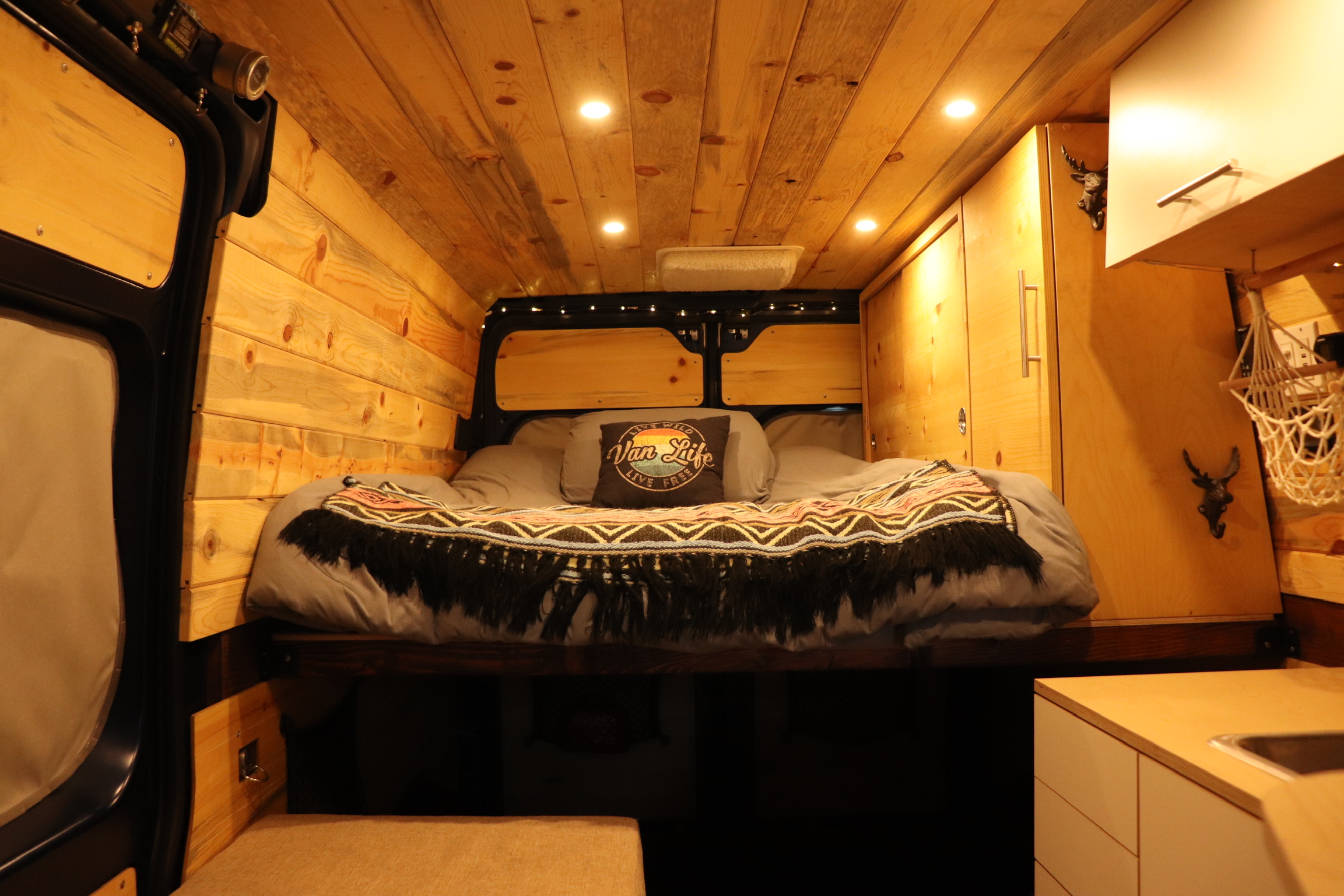 Warm, wood-lined RV rental interior featuring a comfortable bed, cabinets, and a compact kitchen counter.. Ram Promaster 2500 2021