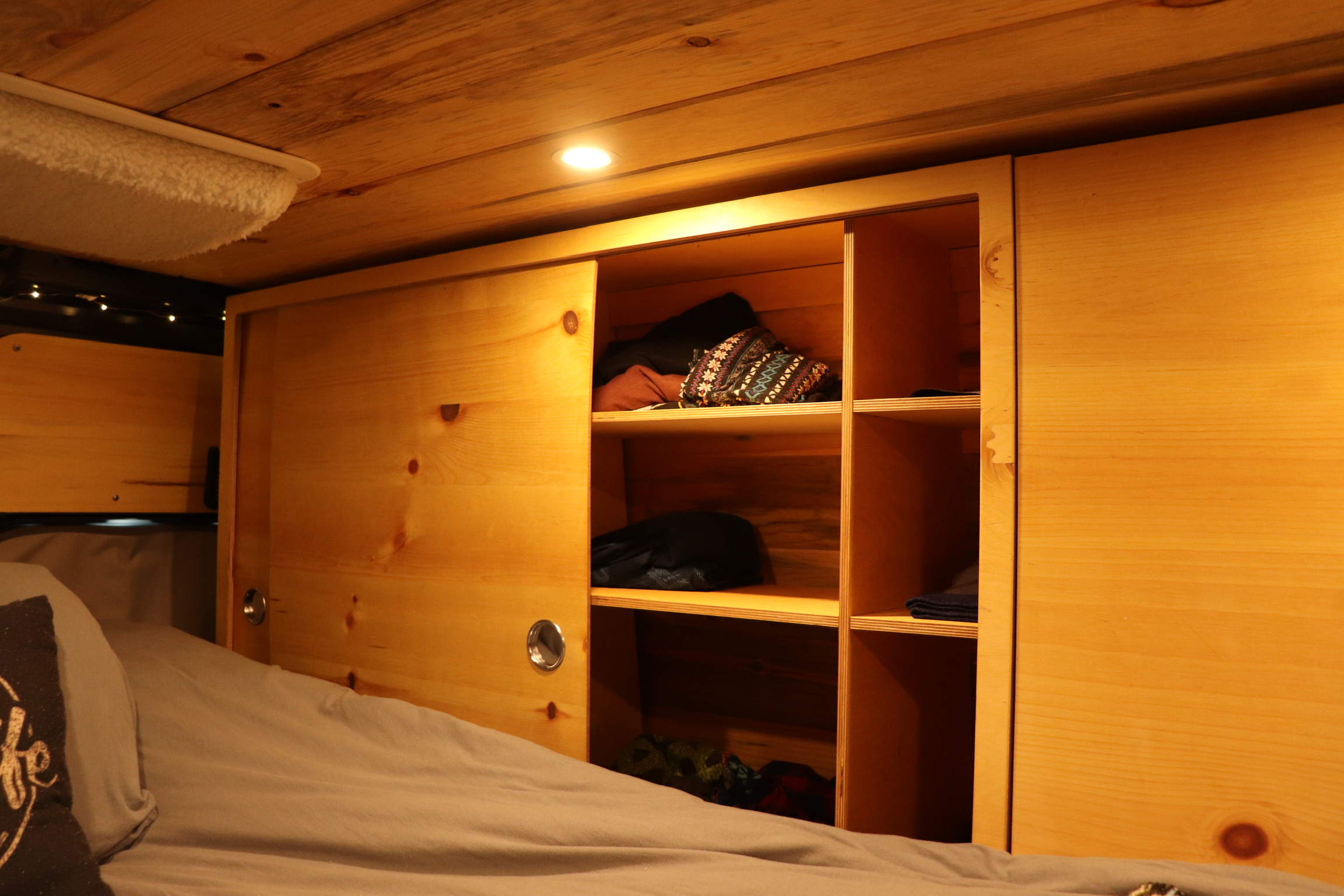 Cozy wooden RV rental interior with a bed, built-in storage with sliding doors, and warm overhead lighting.. Ram Promaster 2500 2021