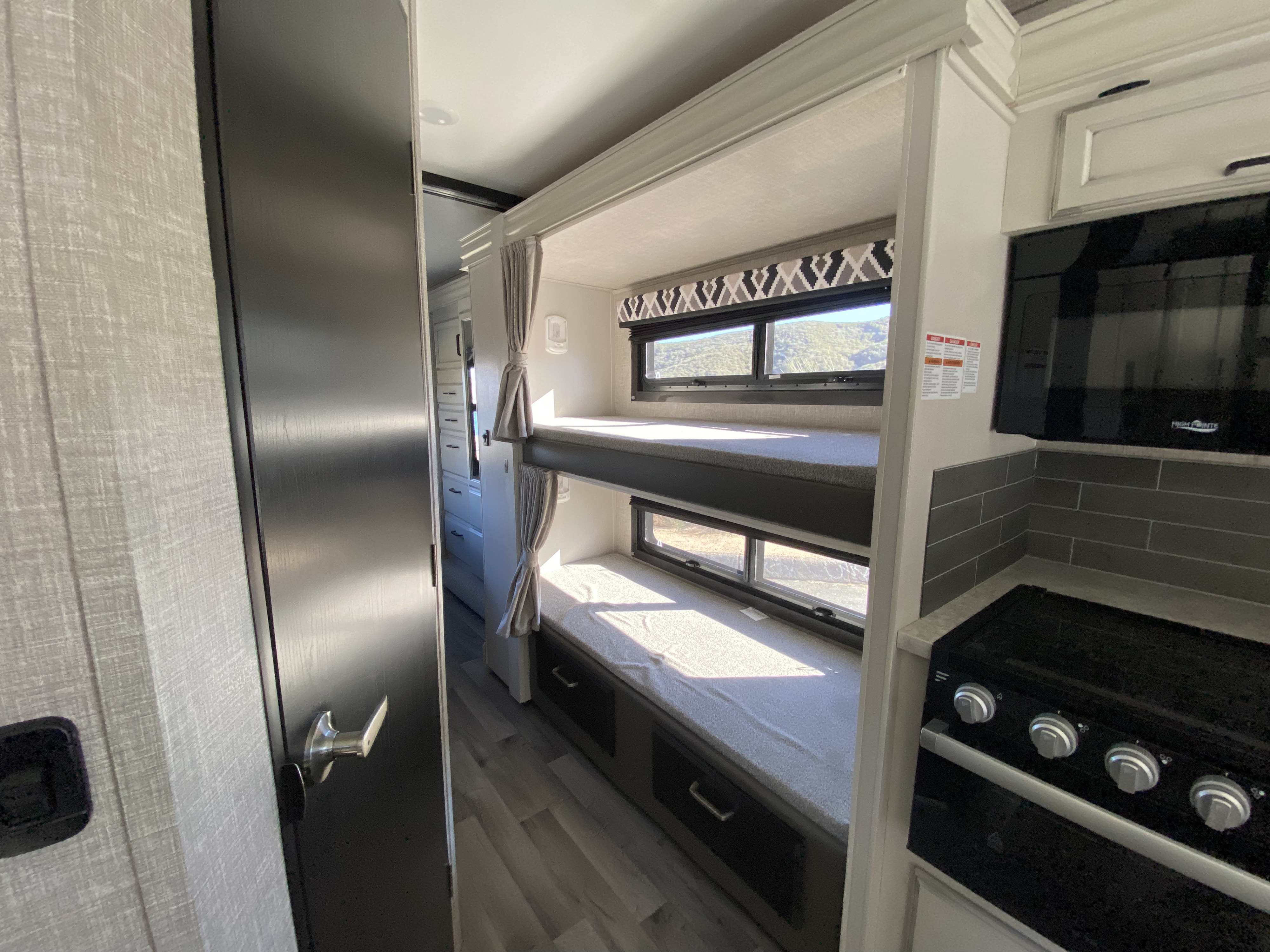Explore this modern RV rental interior featuring cozy bunk beds with windows and a compact kitchen with a stove and microwave.. Jayco Redhawk 2022