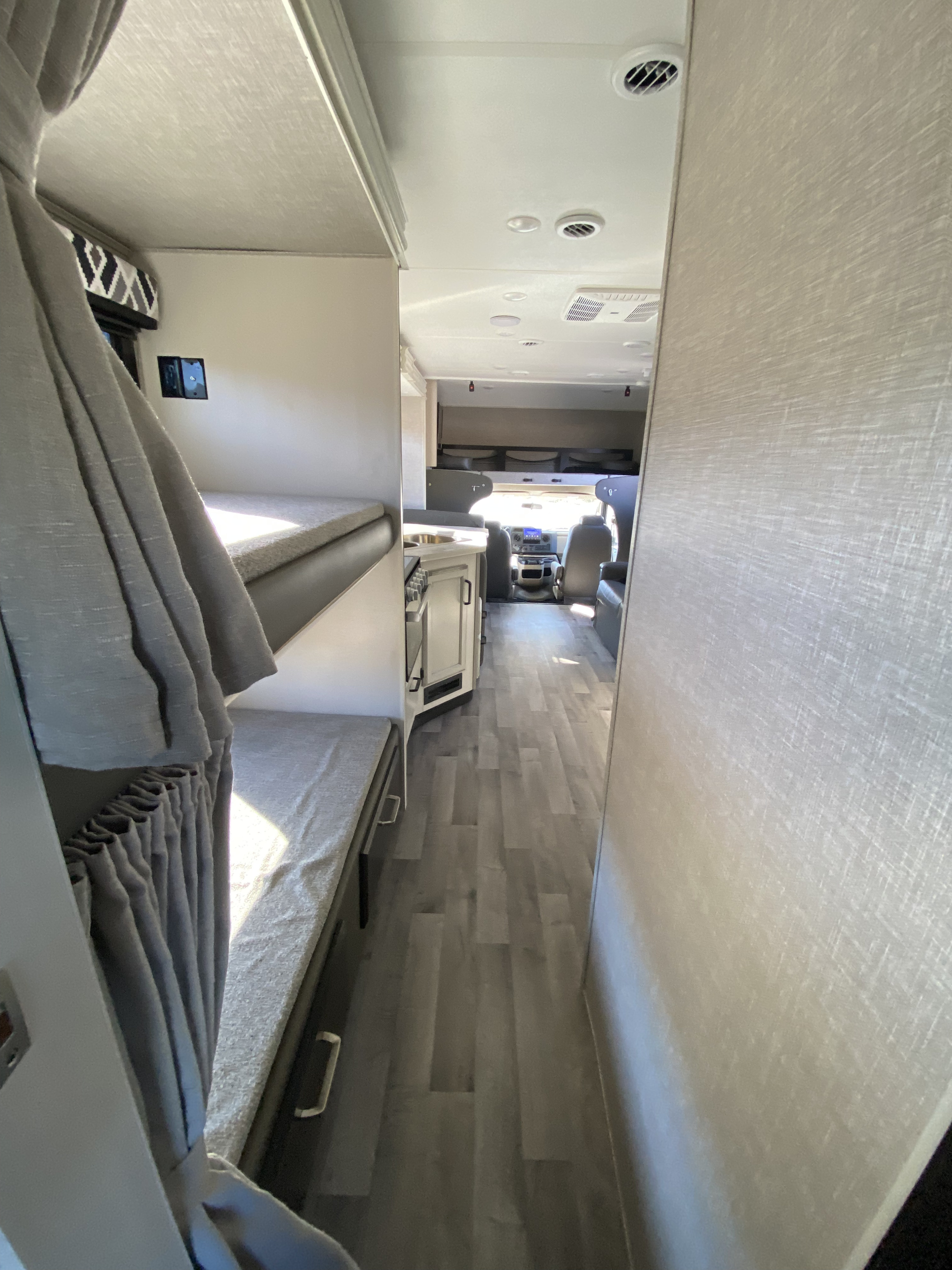 Inside an rv rental, featuring gray bunk beds, a light wood floor, and the cockpit visible ahead. Bright and modern.. Jayco Redhawk 2022
