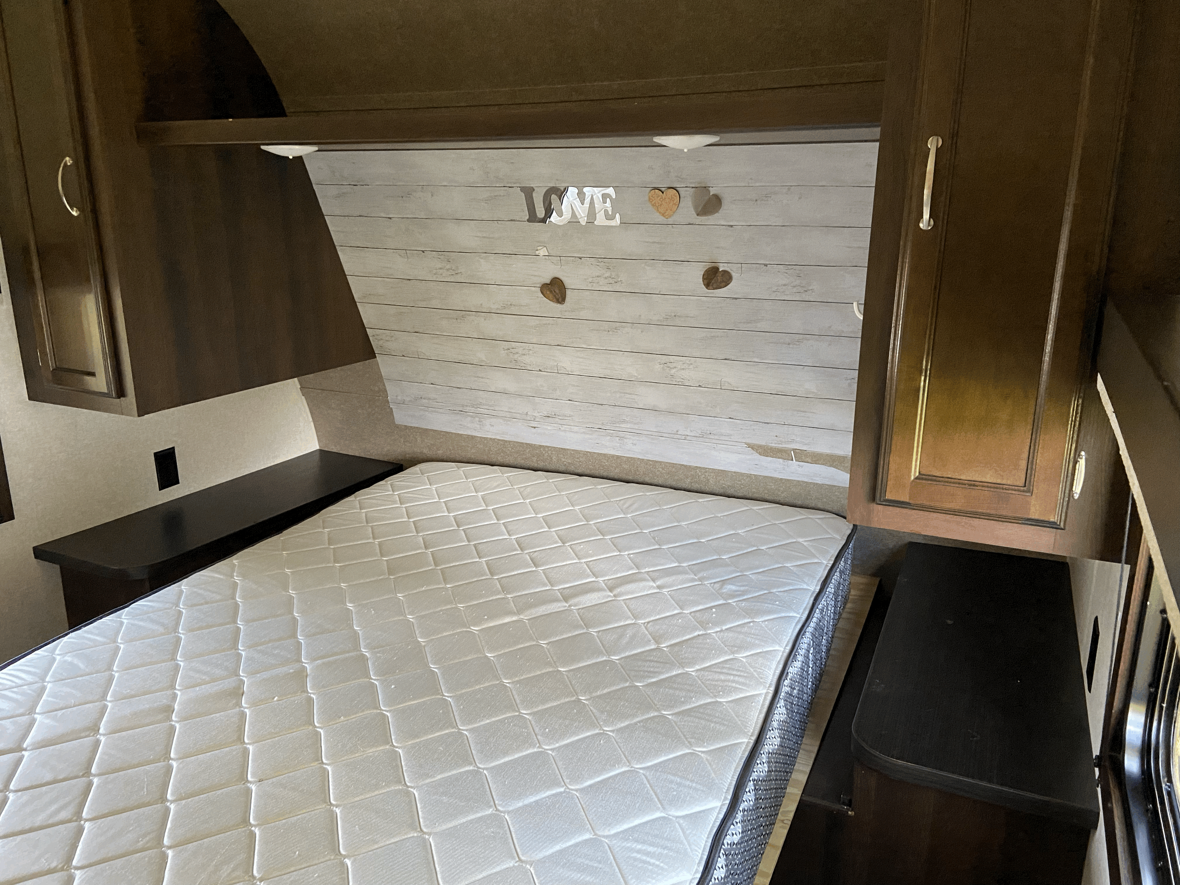 RV rental bedroom featuring a clean white mattress, dark wood cabinetry, and a decorative headboard with "LOVE" letters.. Jayco Jay Feather 2019