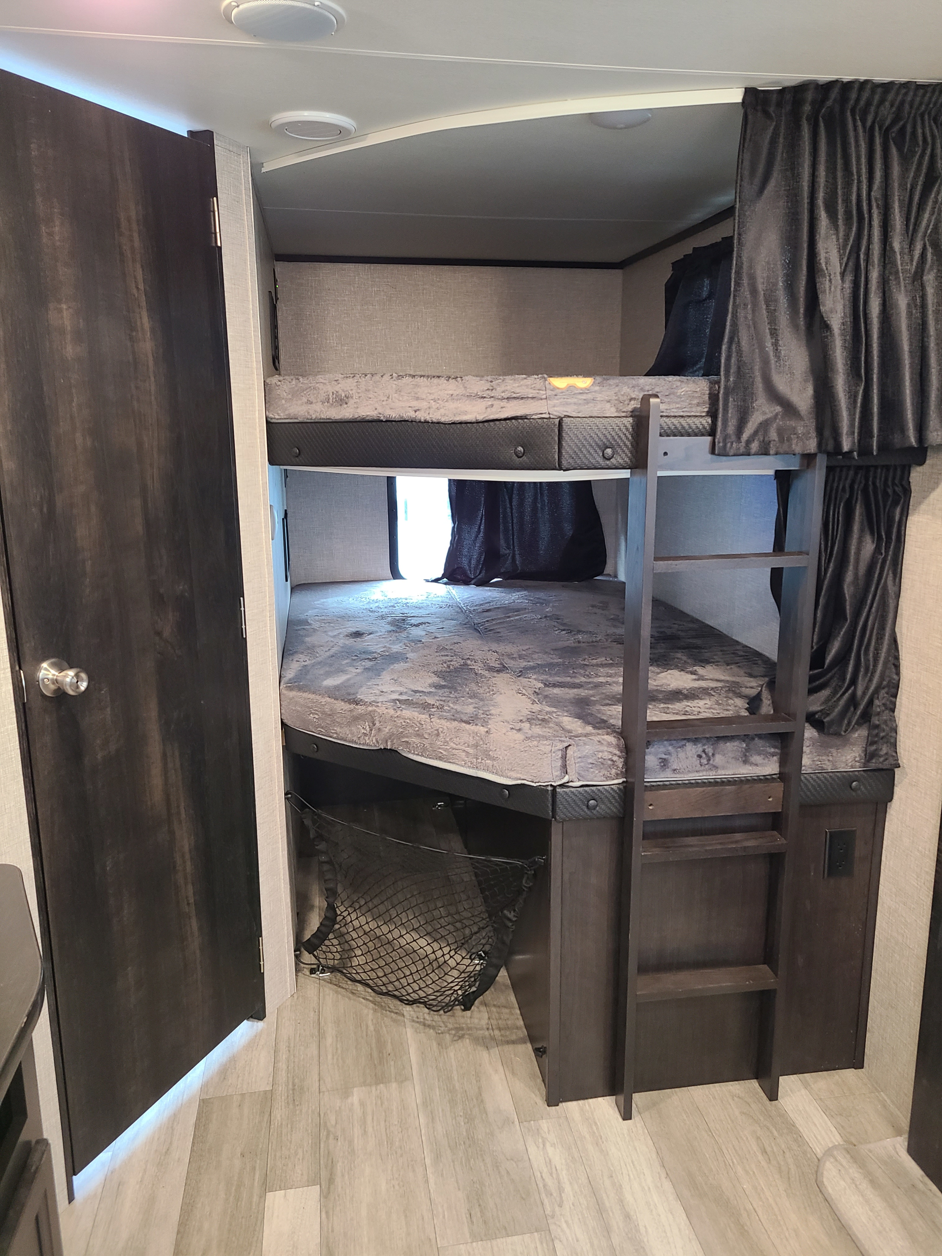 This RV rental interior features a cozy bunk bed setup with privacy curtains, a ladder, and storage, ideal for campers.. Jayco Jay Feather 2022