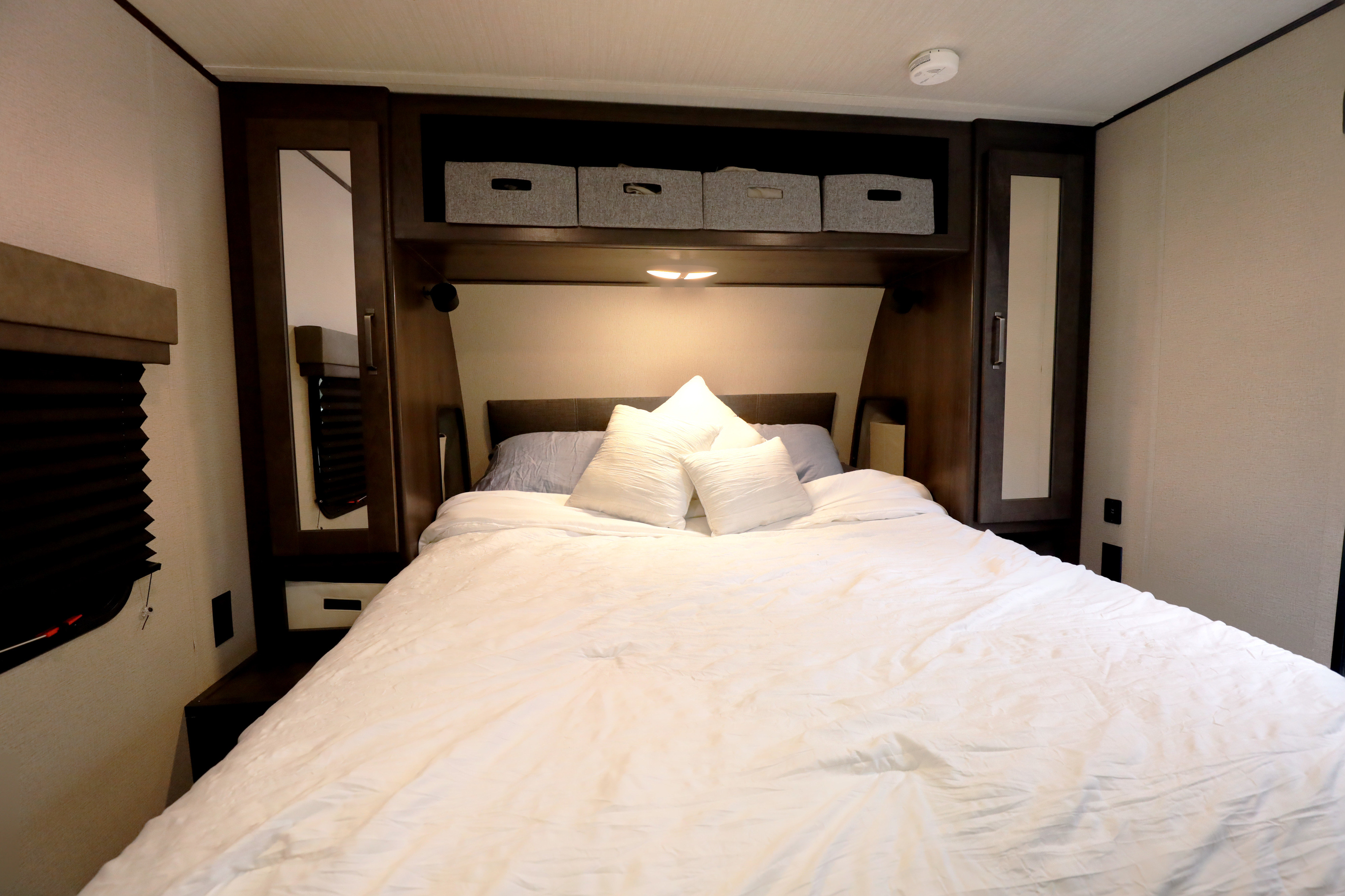 Spacious RV rental bedroom featuring a large bed with white linens, overhead storage, and mirrored cabinets for a comfortable stay.. Grand Design Transcend Xplor 2022