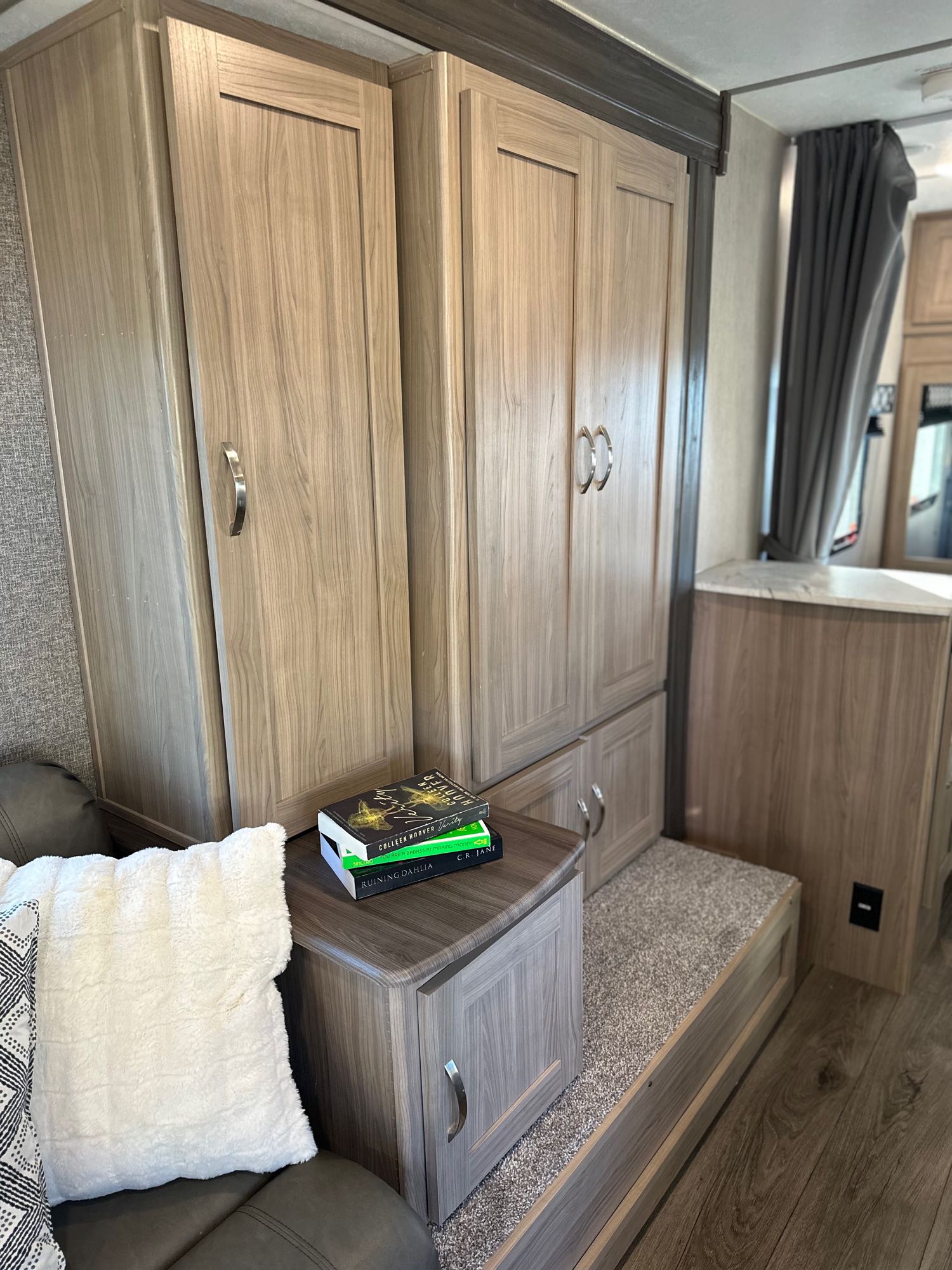 RV rental bedroom area with light wood cabinets, built-in storage, a cozy pillow, and reading books.. Coachmen Freedom Express 2021