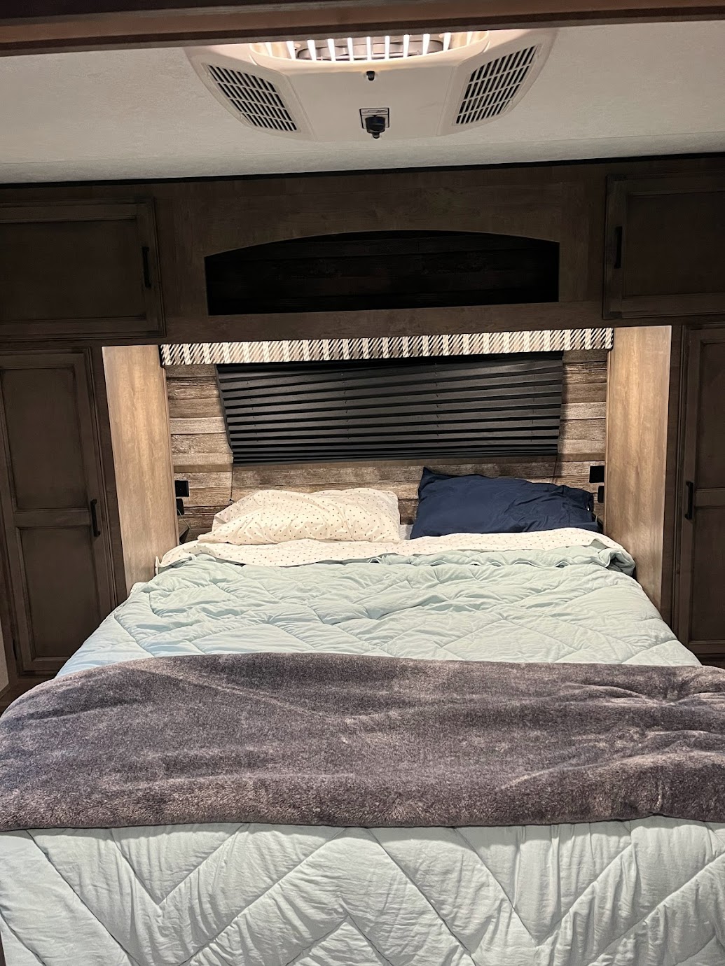 Inside an RV rental bedroom: a comfy bed with blue bedding, built-in storage, and ceiling AC unit.. Venture Stratus 2022