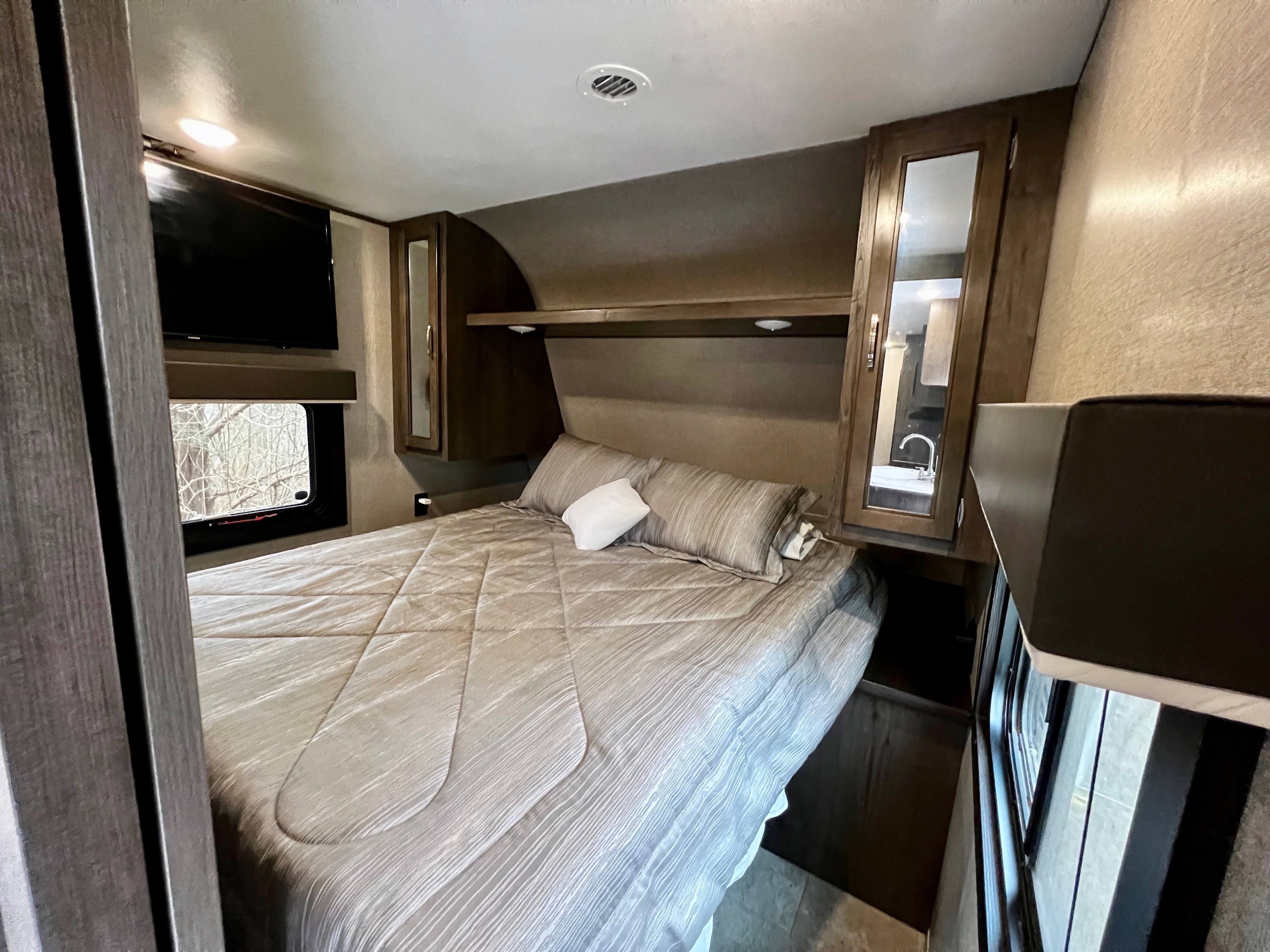 Relax in this RV rental bedroom featuring a comfortable bed, wall-mounted TV, window, and built-in storage.. Jayco Jay Flight SLX 2020