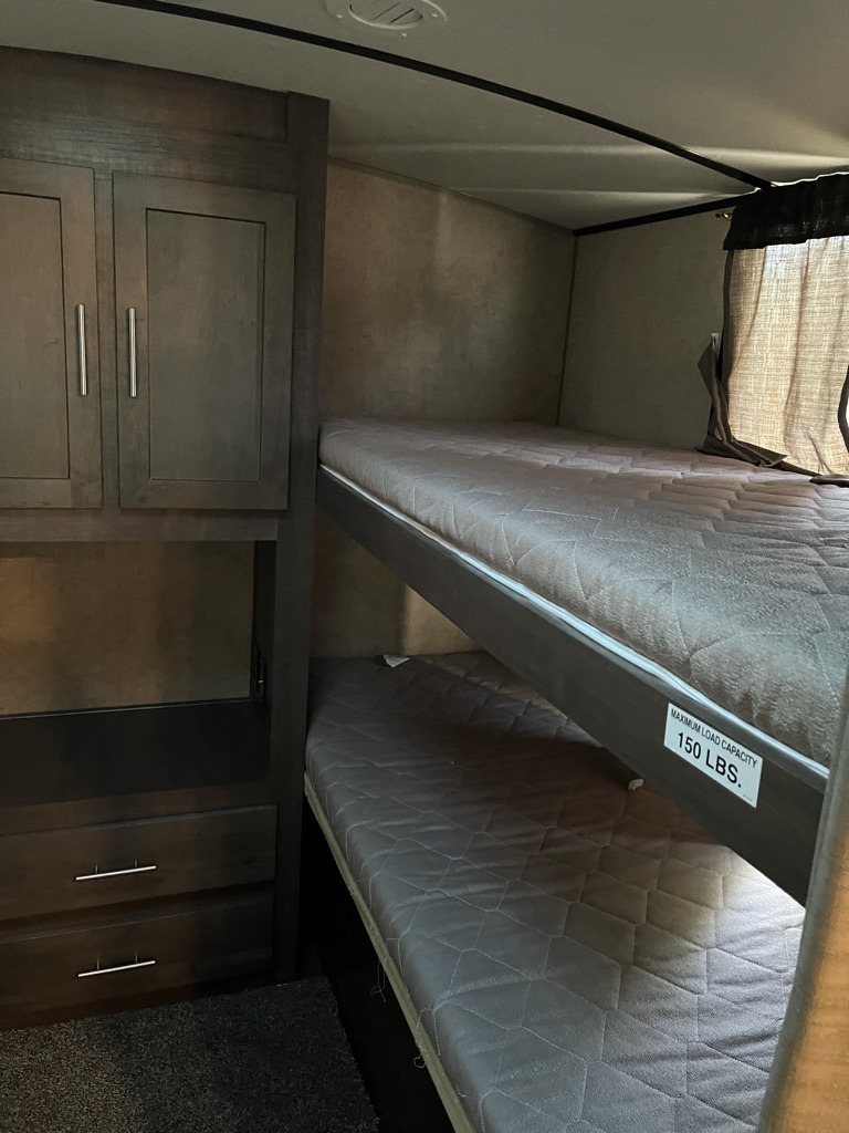 This RV rental features two stacked bunk beds with quilted mattresses and dark wood storage, showing a 150lb weight limit.. Forest River Surveyor 2016