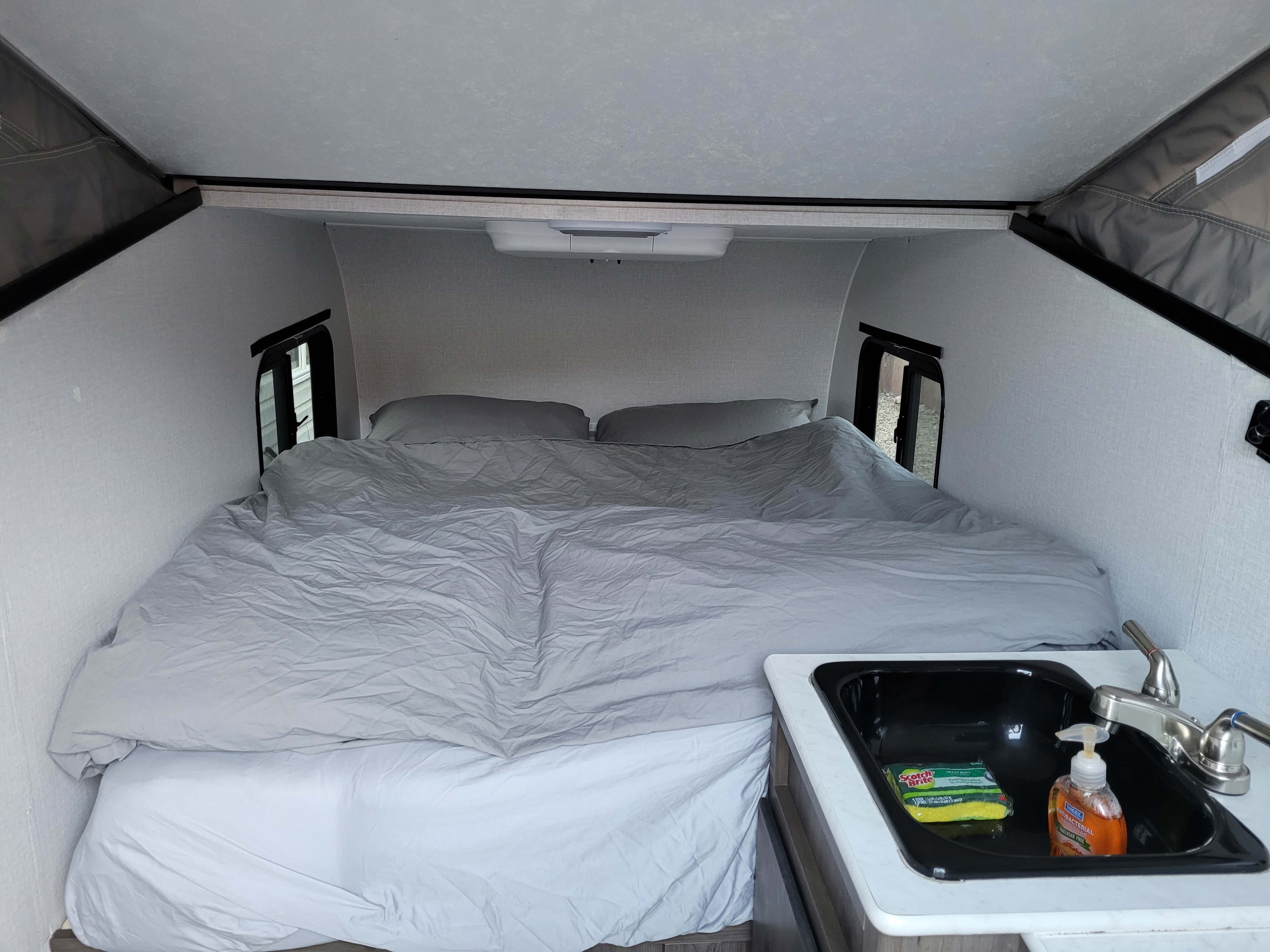 Cozy RV rental interior: pop-up ceiling, spacious bed with gray linens, and compact sink area.. Coachmen Clipper Express 9.0 TD 2022