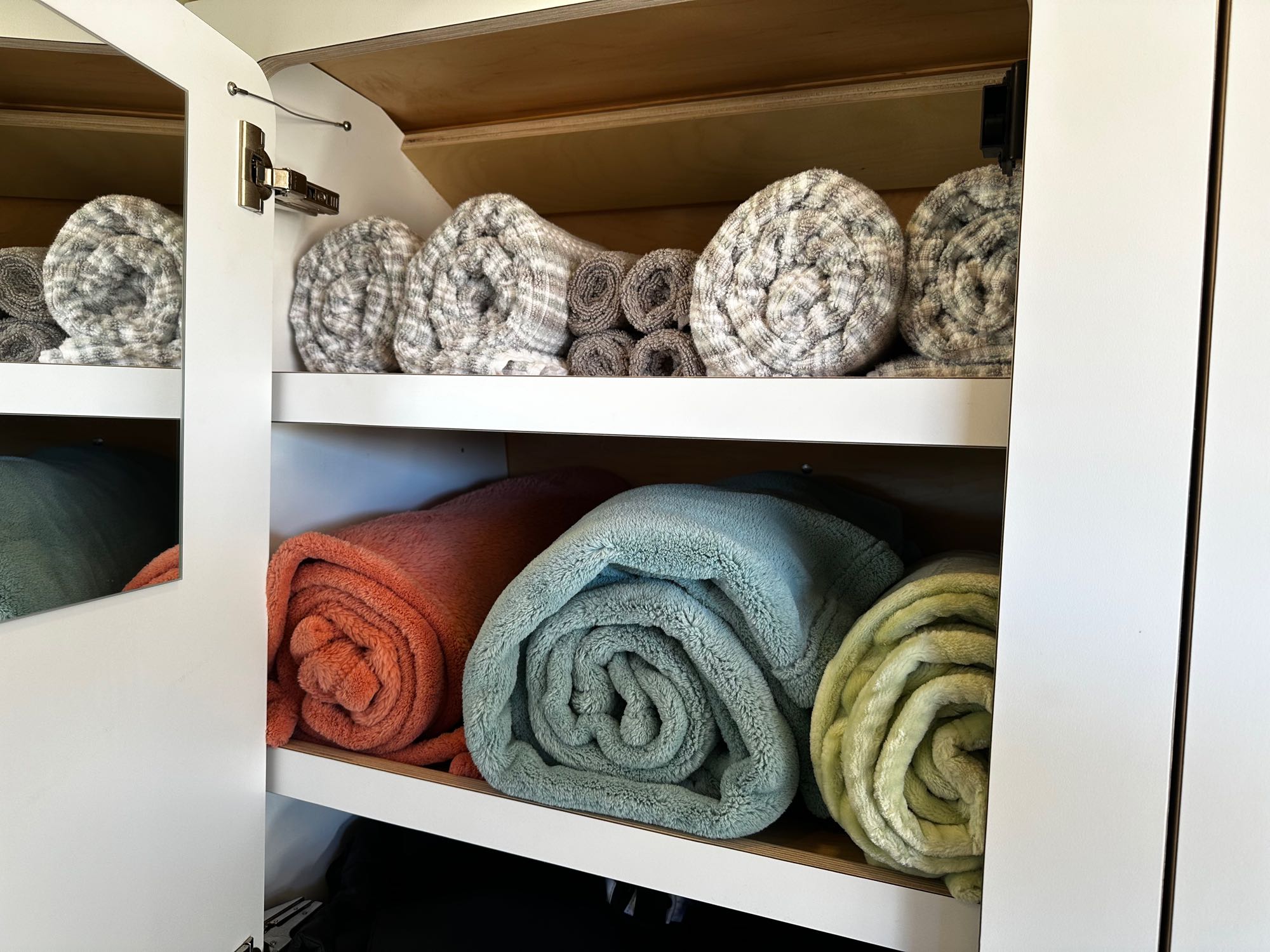 Plush, rolled blankets and throws neatly organized in a built-in cabinet, ready for your comfortable RV rental experience.. VanCraft VanCraft Class B 2022