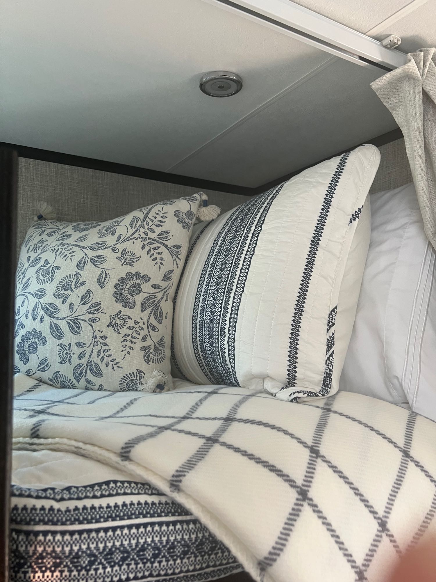 Cozy RV rental interior: A bed with blue & white floral/striped pillows and a plaid blanket. Comfortable bedding for travel.. Jayco 171BH 2023