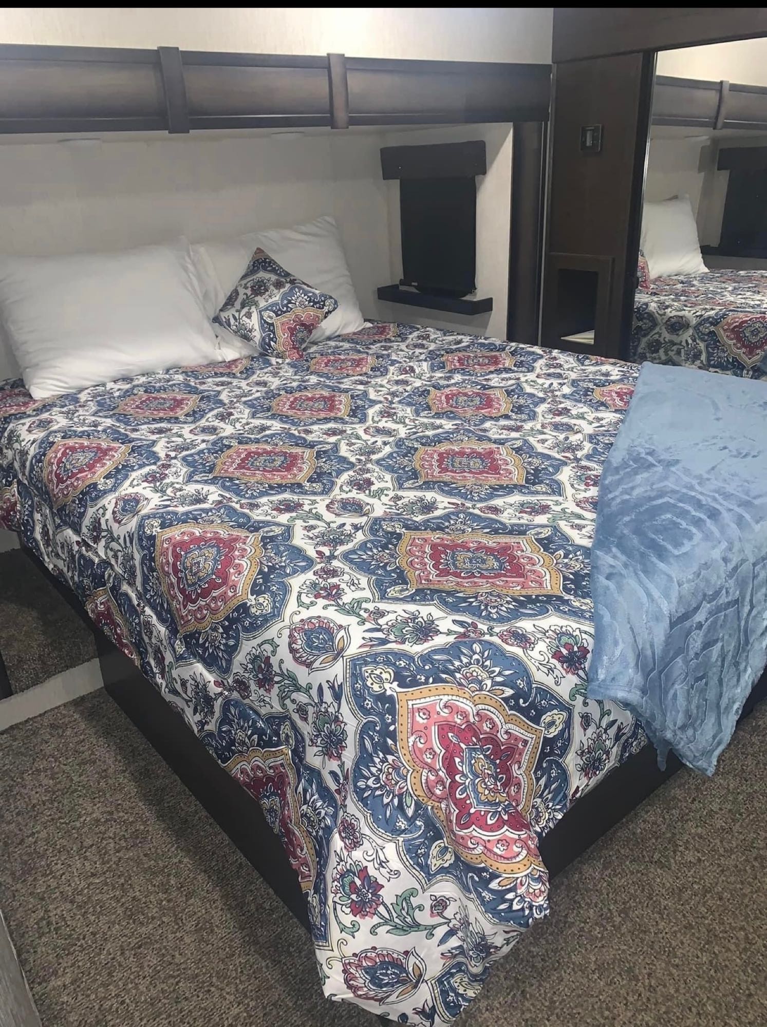 Cozy RV rental bedroom with a colorful duvet, plush pillows, and a soft blue throw, inviting for travel comfort.. Heartland Elkridge 2019