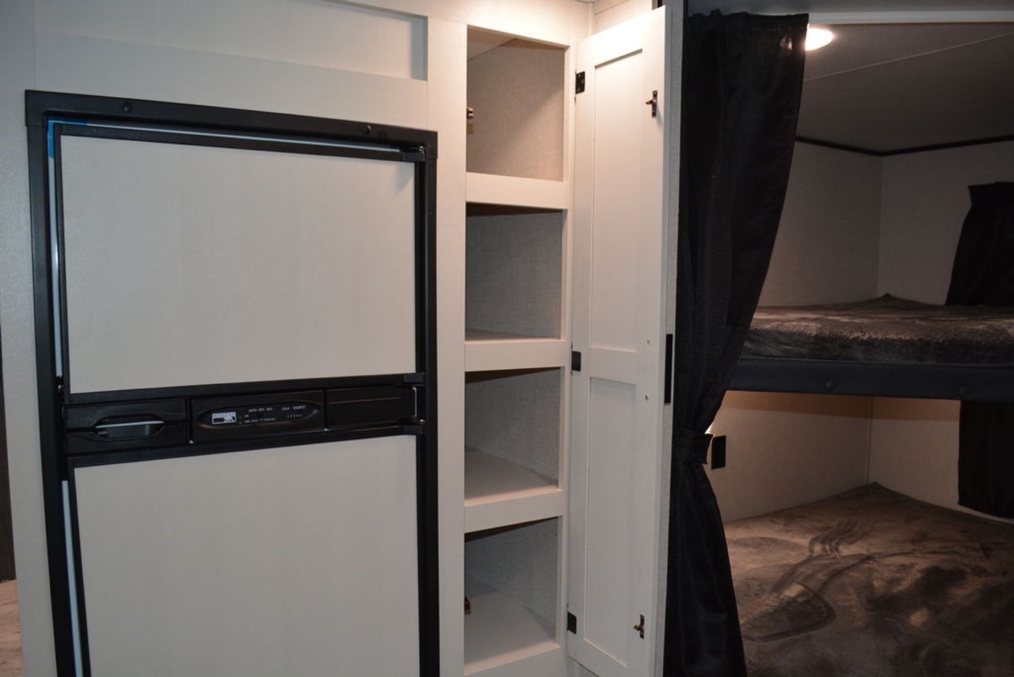 RV rental interior: fridge, shelving, and cozy bunk beds with privacy curtains. Ideal for family trips.. Highland Ridge RV Open Range 2022