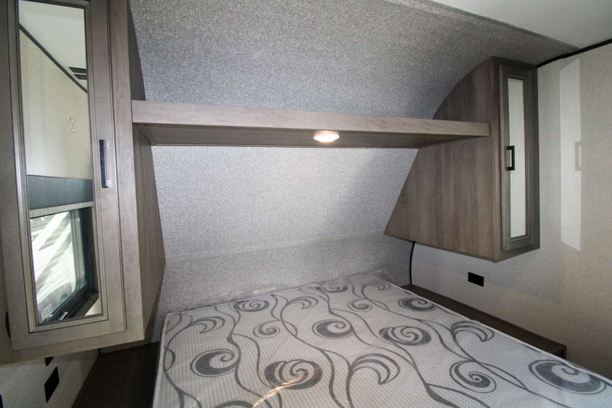 RV rental bedroom: features a patterned bed, overhead shelf with light, and mirrored wall cabinets for storage.. Highland Ridge RV Open Range 2022