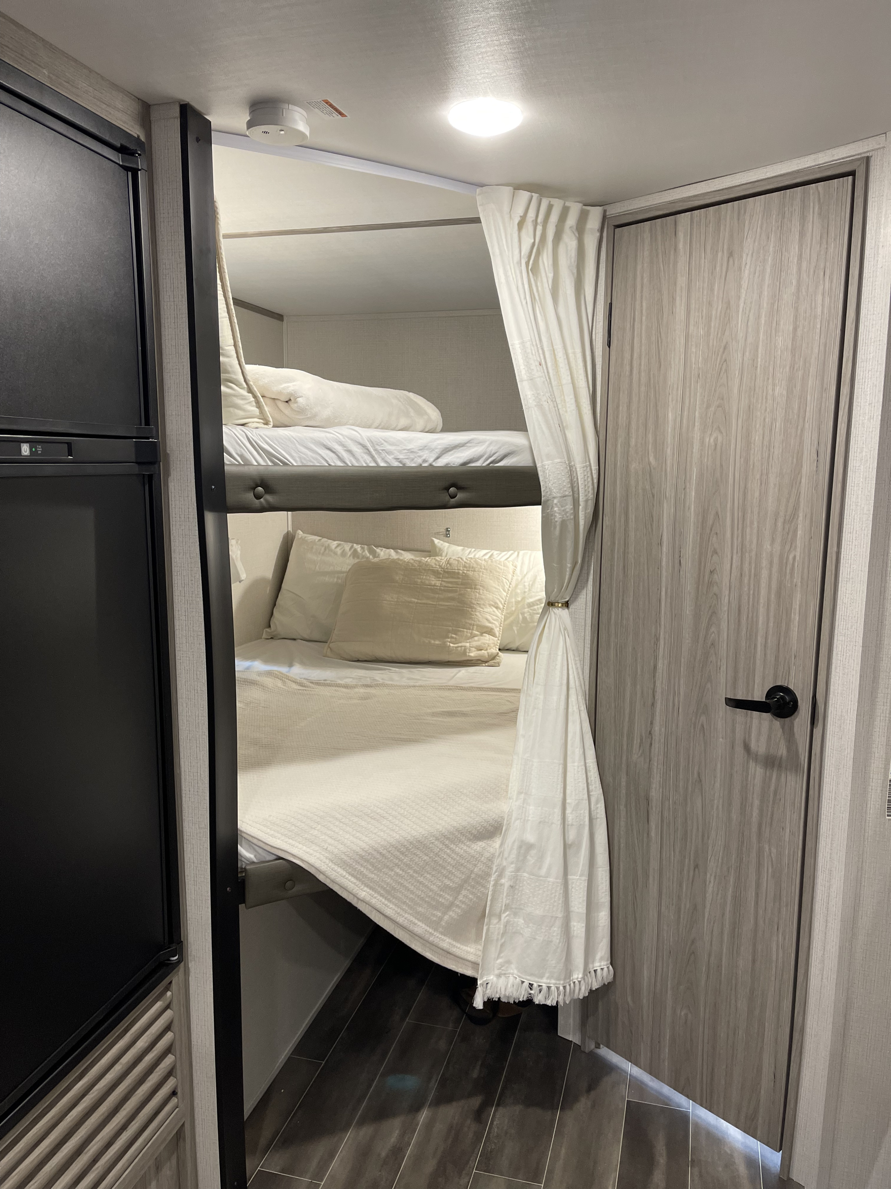 Cozy RV rental interior featuring comfortable bunk beds with privacy curtains, a refrigerator, and a light-colored wood door.. Keystone RV Passport SL 2022