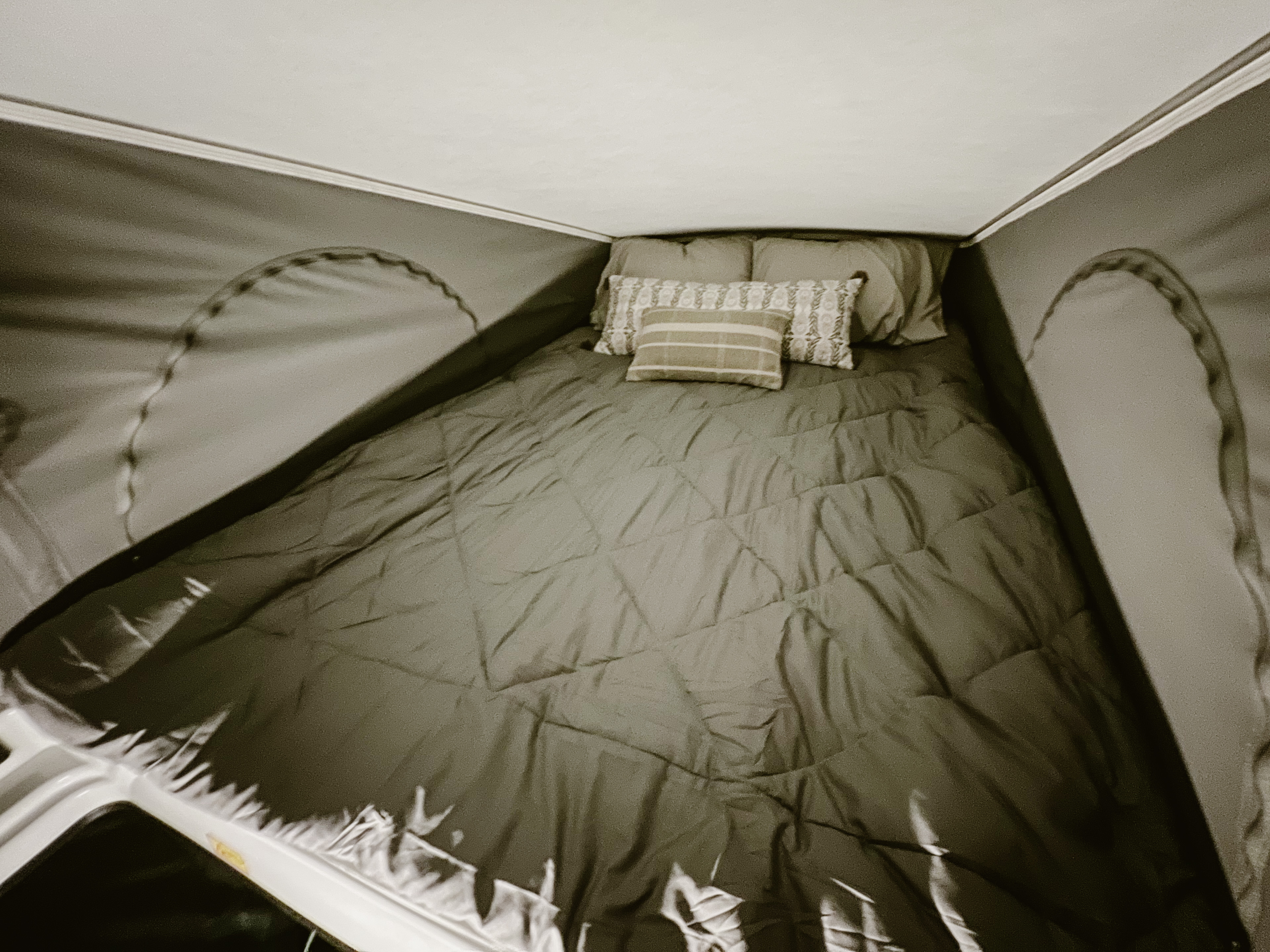Cozy RV rental pop-top bed, perfect for travel. Dark comforter and pillows on a comfortable mattress inside a camper.. Winnebago Solis 59PX 2023