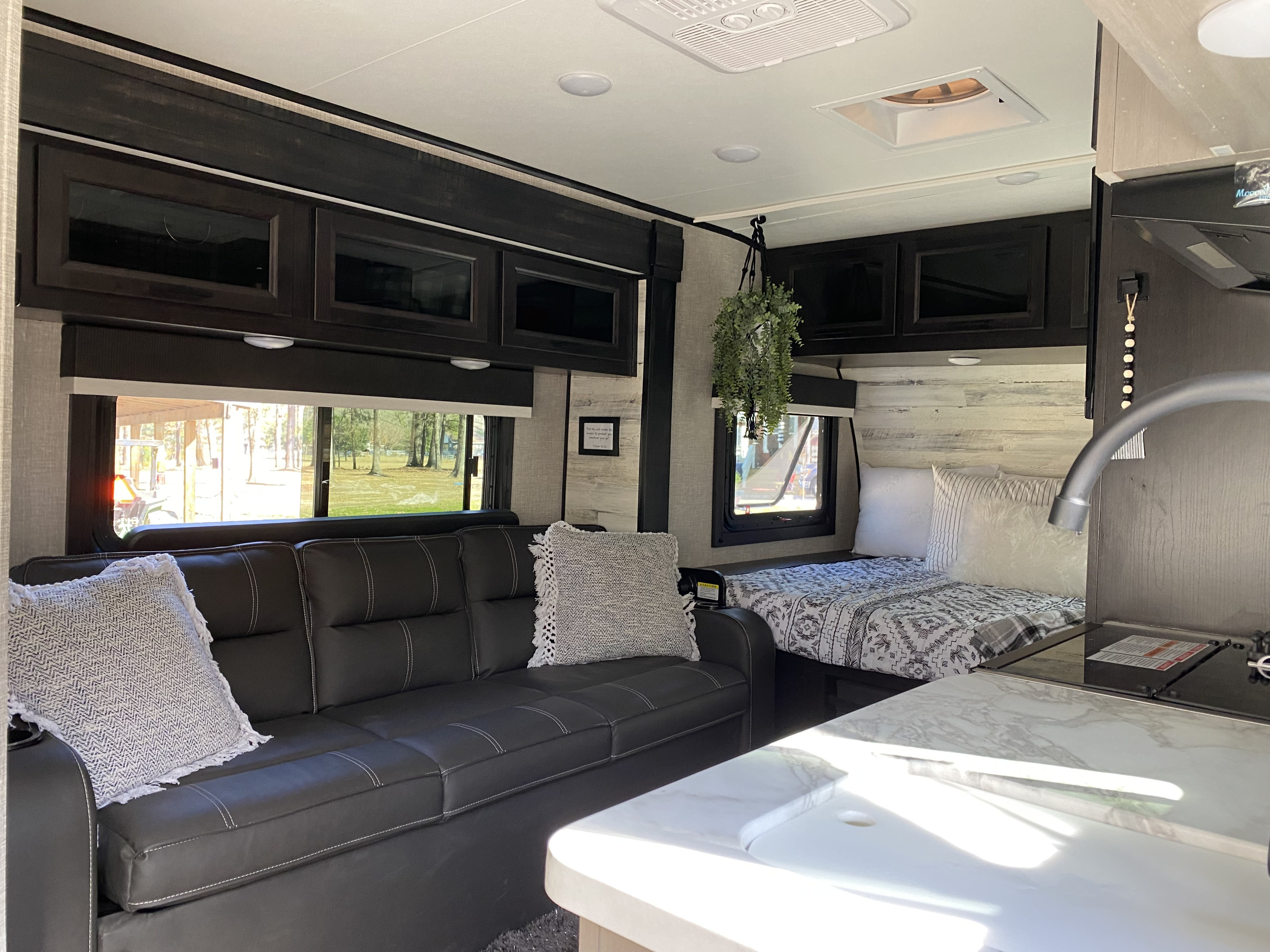 Interior of a modern RV rental, featuring a dark sofa, light bedding, and kitchen counter with a sink.. Jayco Jay Feather Micro 2022