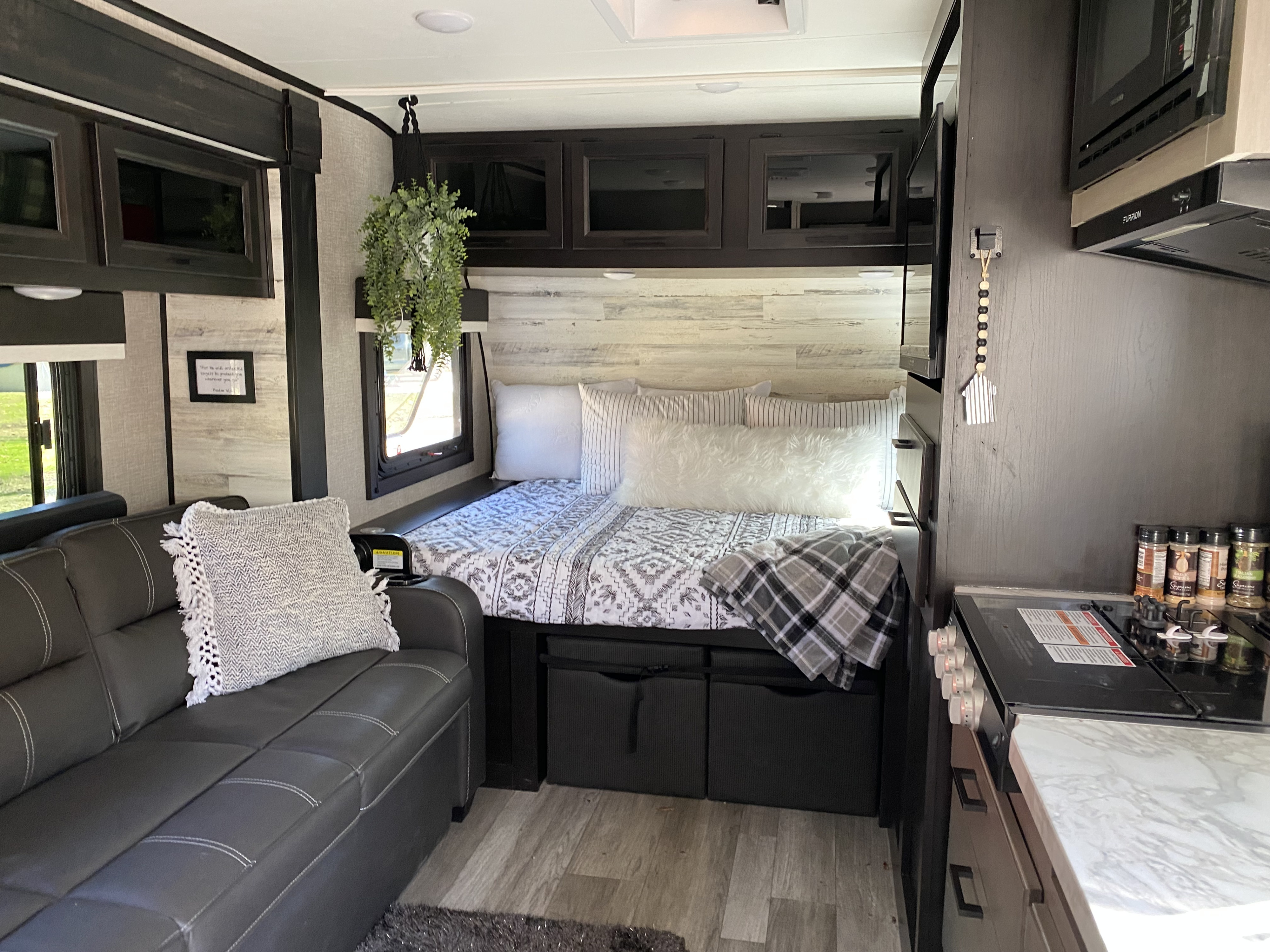 Cozy RV rental interior: bed with patterned bedding, couch, dark cabinets, kitchen area, and wood-look flooring.. Jayco Jay Feather Micro 2022