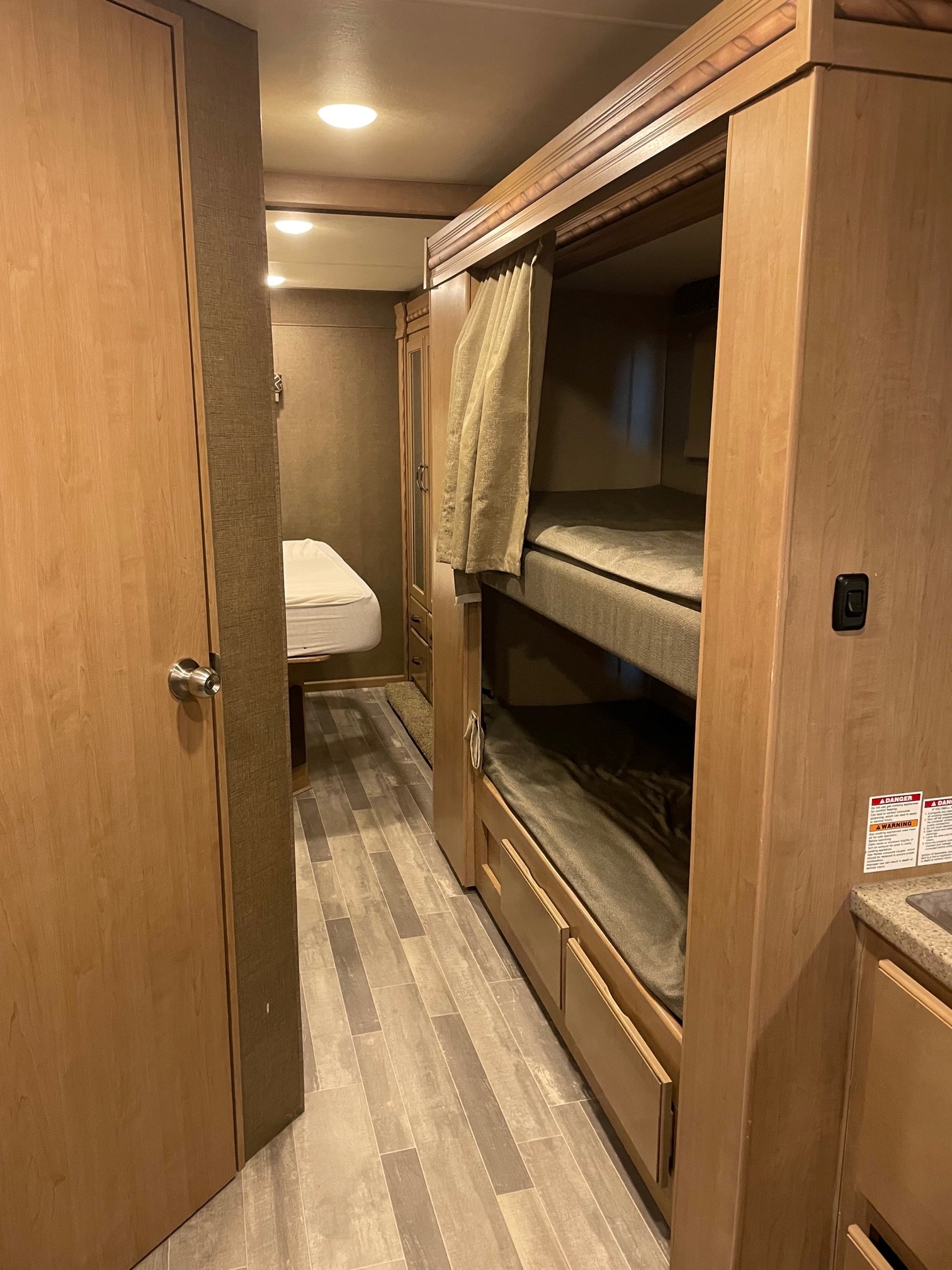 Cozy rv rental interior featuring bunk beds on the right, a private bedroom straight ahead, and wood-look flooring.. Thor Motor Coach Four Winds 2018