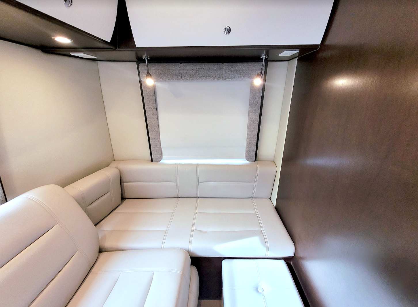 Cozy RV rental lounge featuring a cream convertible sofa, window, and task lighting. Ideal for relaxation in your mobile home.. Leisure Travel Serenity 2016