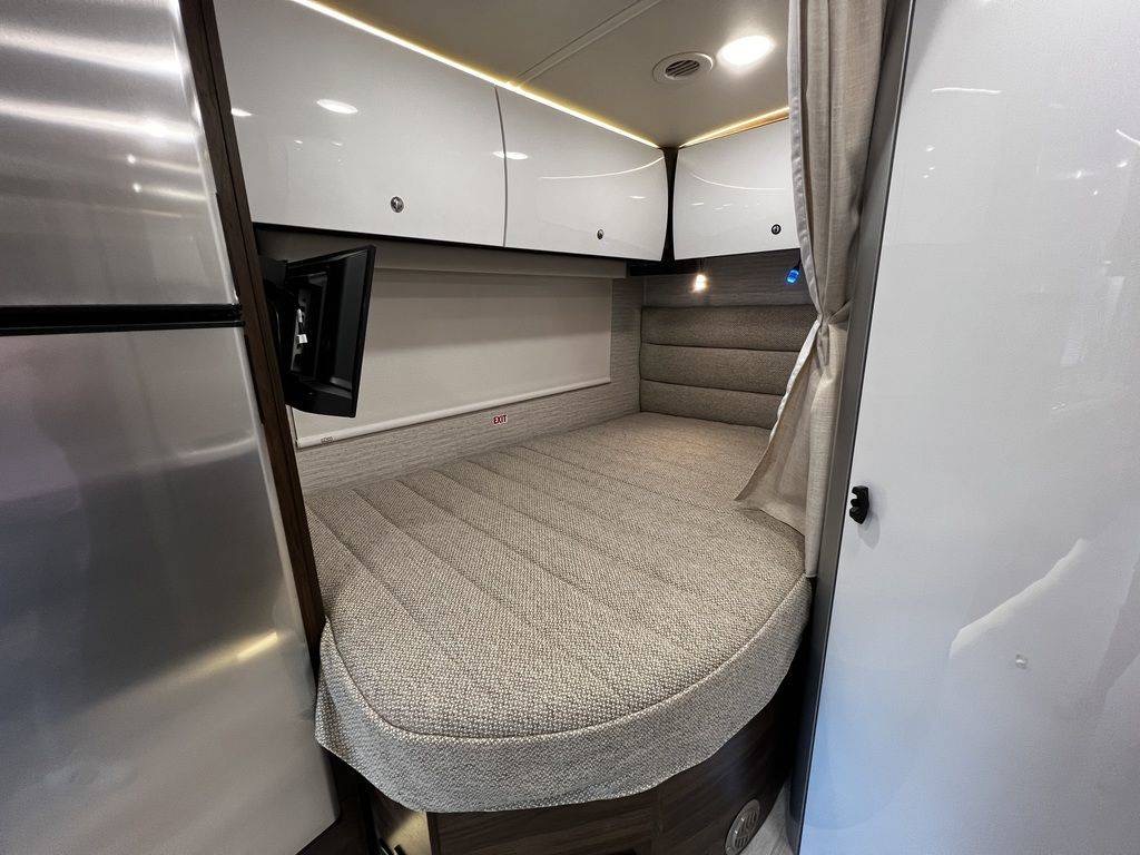 Cozy RV rental sleeping space: compact bed, mounted TV, sleek storage, and privacy curtain. Ideal camper interior.. Winnebago View 2022