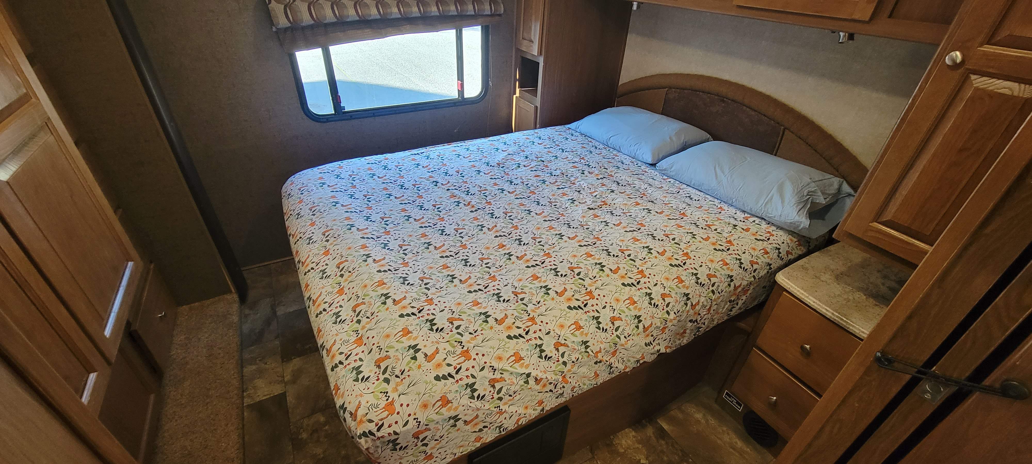 An inviting RV rental bedroom with a comfy bed, nature-themed bedding, and practical wooden storage, perfect for your journey.. Coachmen Leprachaun 320BH 2017