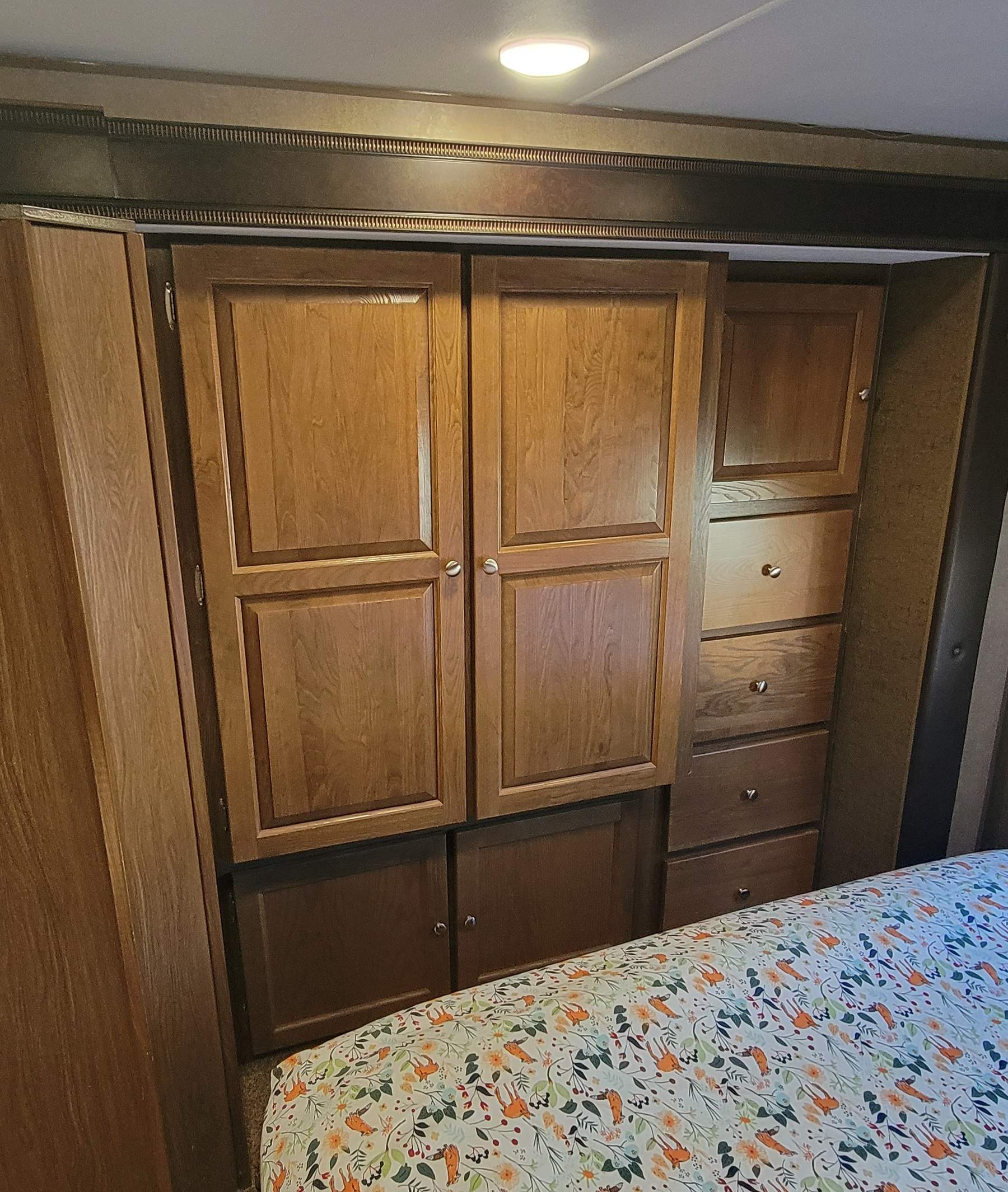 RV rental bedroom: Wood cabinets, drawers & a bed with cheerful sheets offer compact storage in this cozy RV interior.. Coachmen Leprachaun 320BH 2017