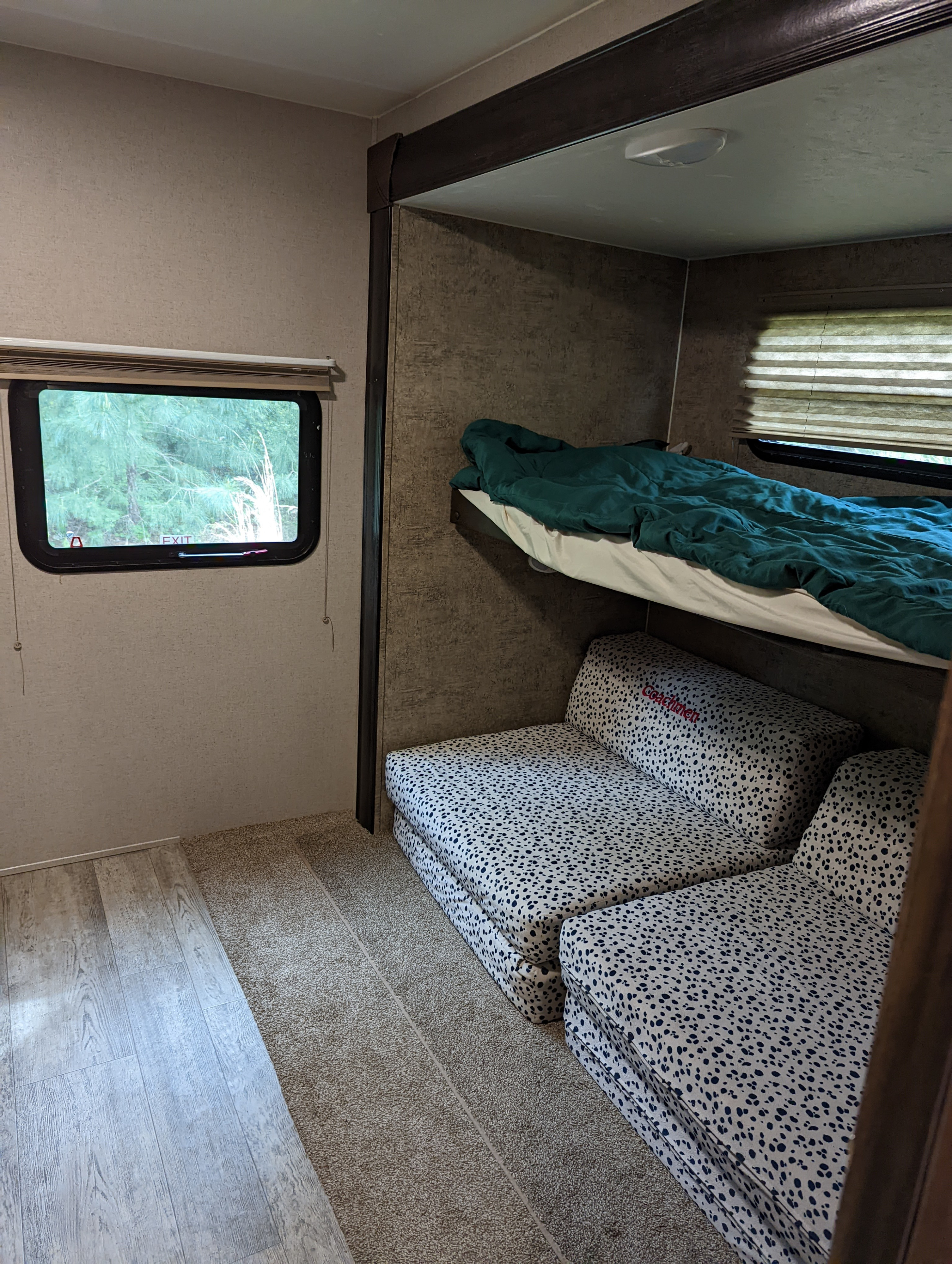 Cozy RV rental interior with bunk beds: top with green blanket, lower spotted cushions, window to trees. Ideal for travel.. Forest River Coachmen Freedom Express 2017