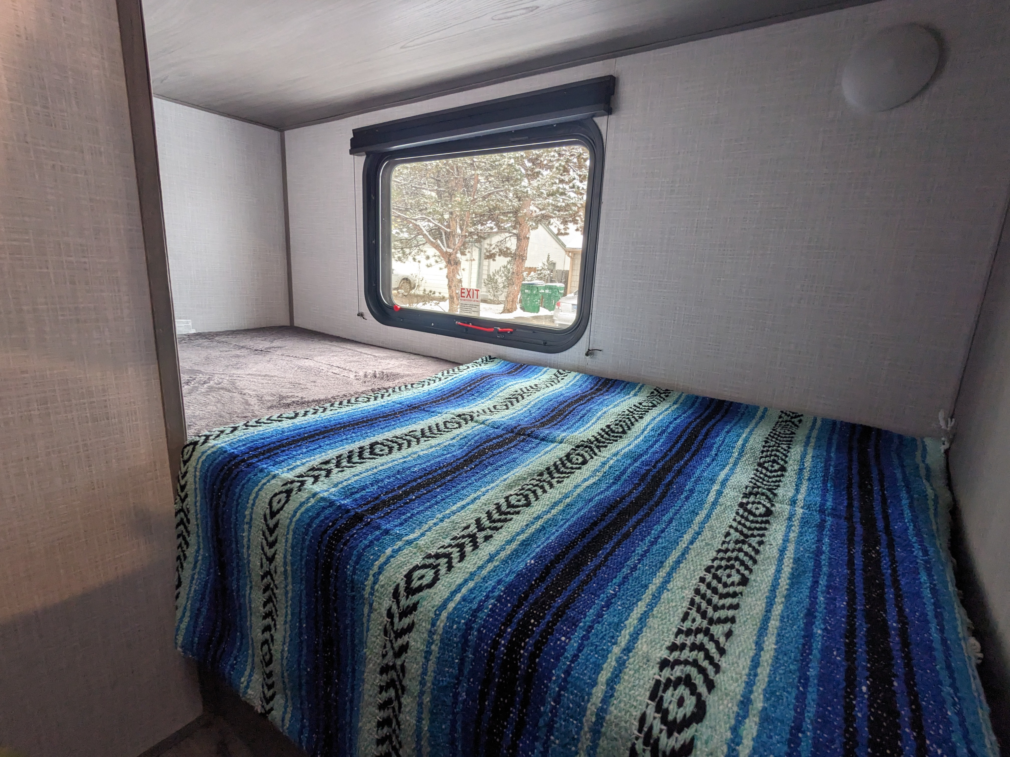 Cozy RV rental bunk beds, one with a blue striped blanket, offer a snowy window view. Ideal camper sleeping area.. Dutchmen Coleman Lantern LT 2022