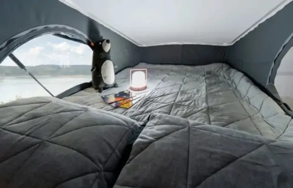 Inside a comfortable RV rental pop-top: a quilted bed, plush toy, glowing lamp, and a stunning lake view.. Winnebago Solis 2021