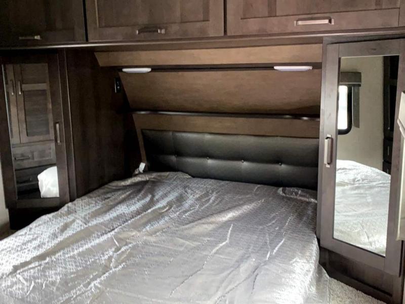 Explore the compact bedroom of this RV rental. Features a bed, mirrored closets, and overhead cabinets.. Grand Design Reflection 2021