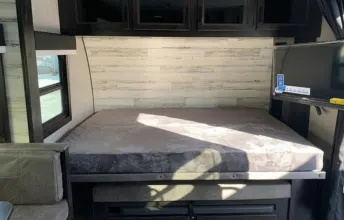 RV rental interior: A cozy bed with a light wood accent wall, dark overhead cabinets, and a TV for comfortable travel.. Jayco Jay Feather Micro 2022