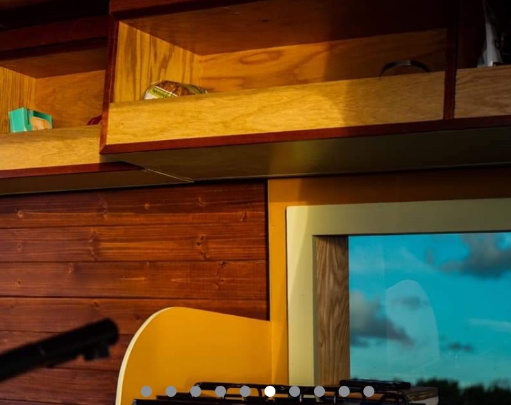 Cozy RV rental interior: wooden cubbies, a window revealing blue sky, and a guitar for travel tunes.. Mercedes Sprinter 2013