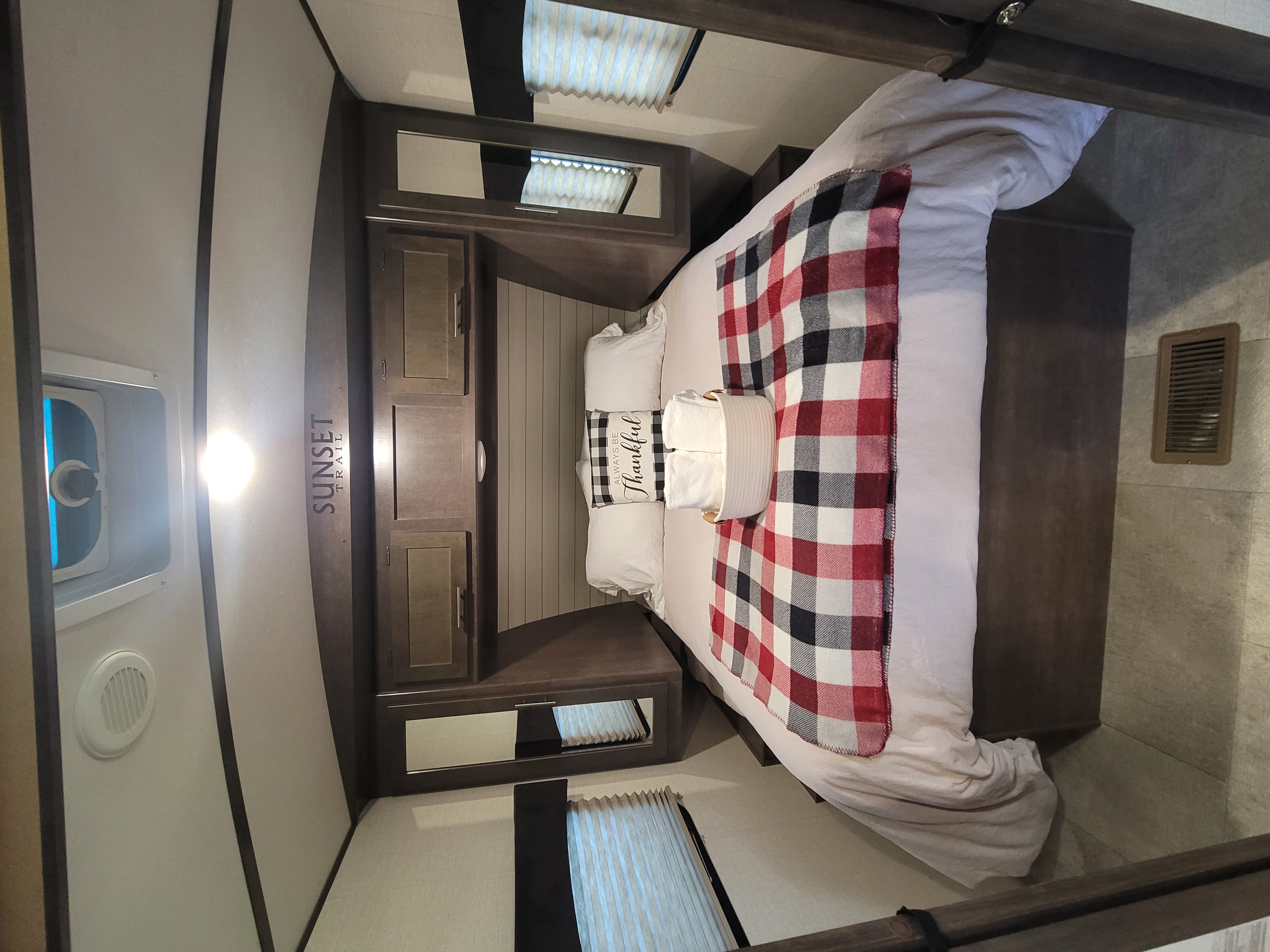 Cozy Sunset Trail RV rental bedroom with a plaid bed, ample storage, and warm lighting for a comfortable stay.. Crossroads RV Sunset Trail Super Lite 2018