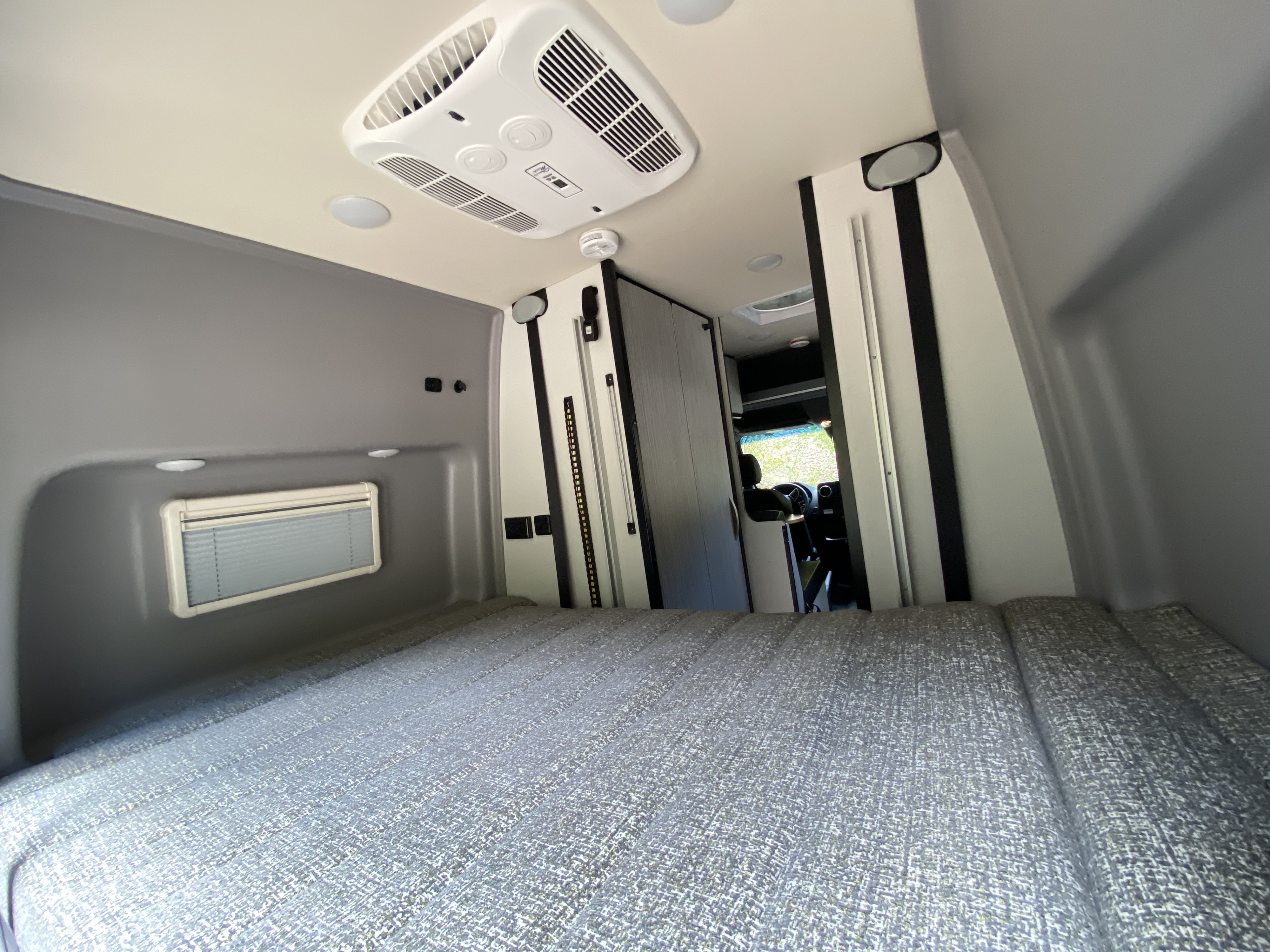 Spacious RV rental interior: comfortable bed, ceiling AC, lighting, and a view to the front cabin. Perfect for travel.. Winnebago Revel 2022