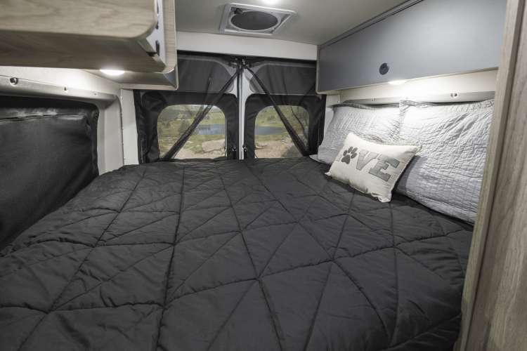 This RV rental's comfy bedroom features a large bed, overhead storage, and rear windows with a nature view.. Winnebago Solis PX 2023